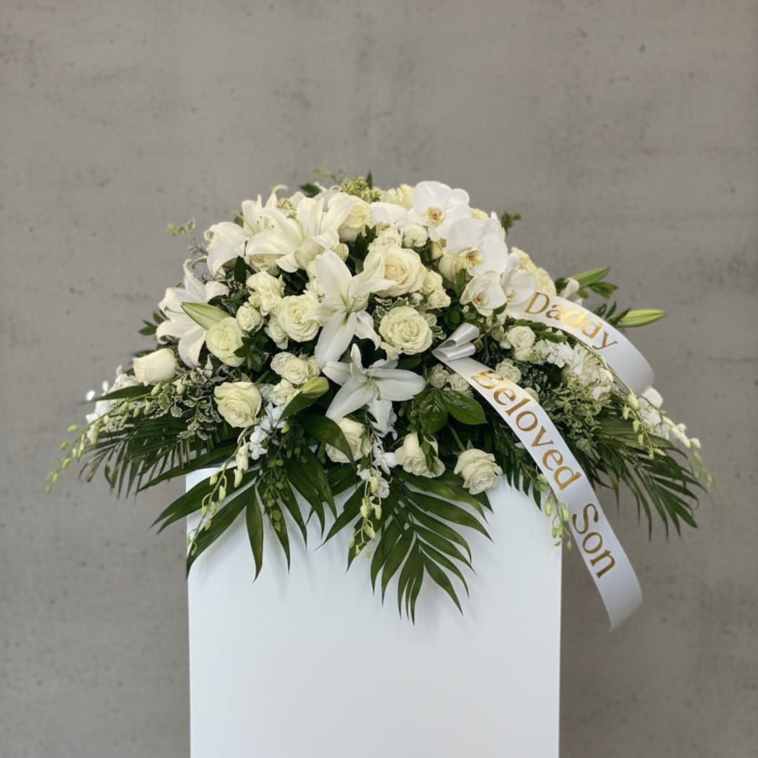 White floral funeral spray with lilies, roses, and orchids on a stand