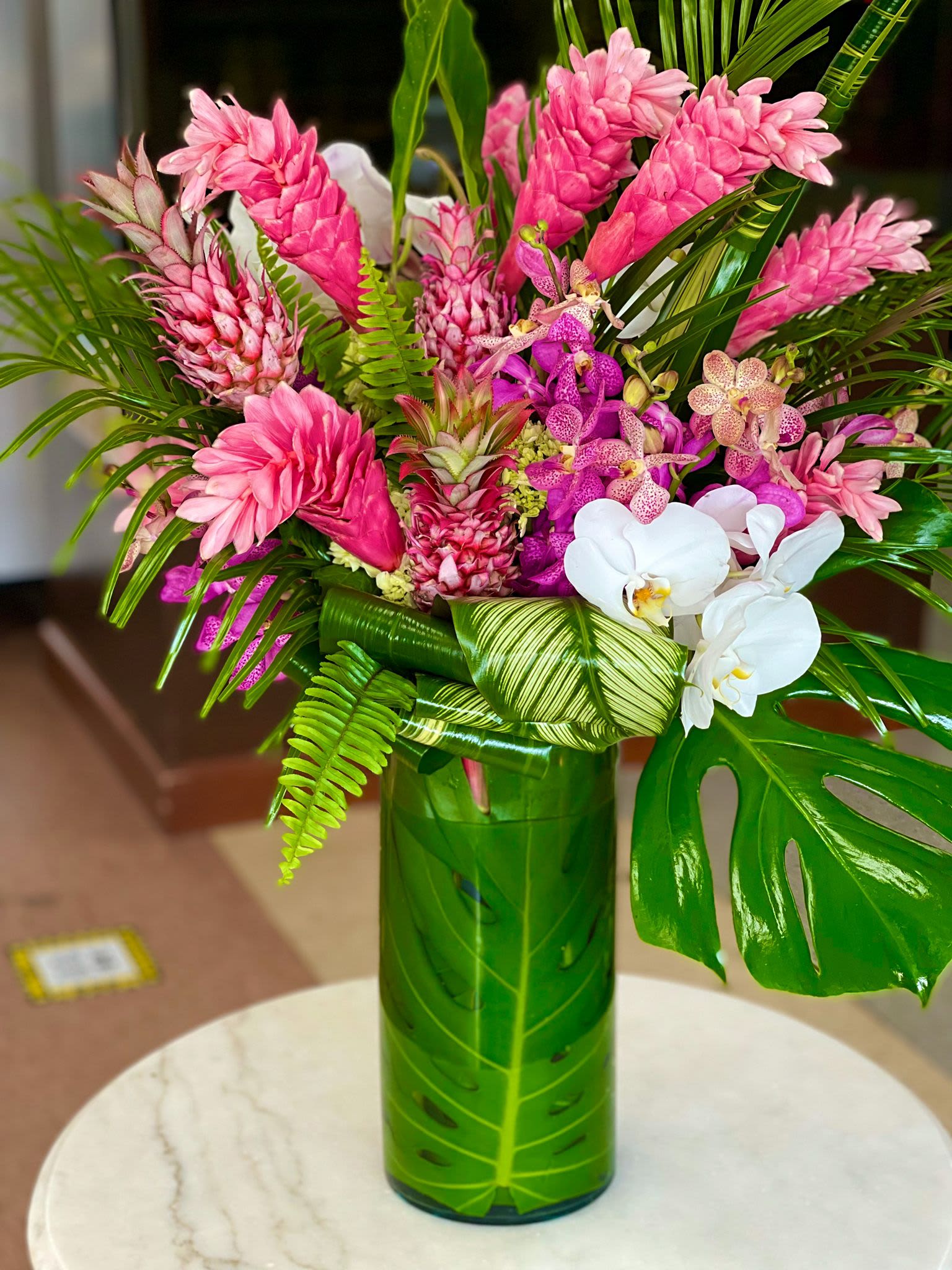 Pink tropical flowers arranged in a green vase with white orchids