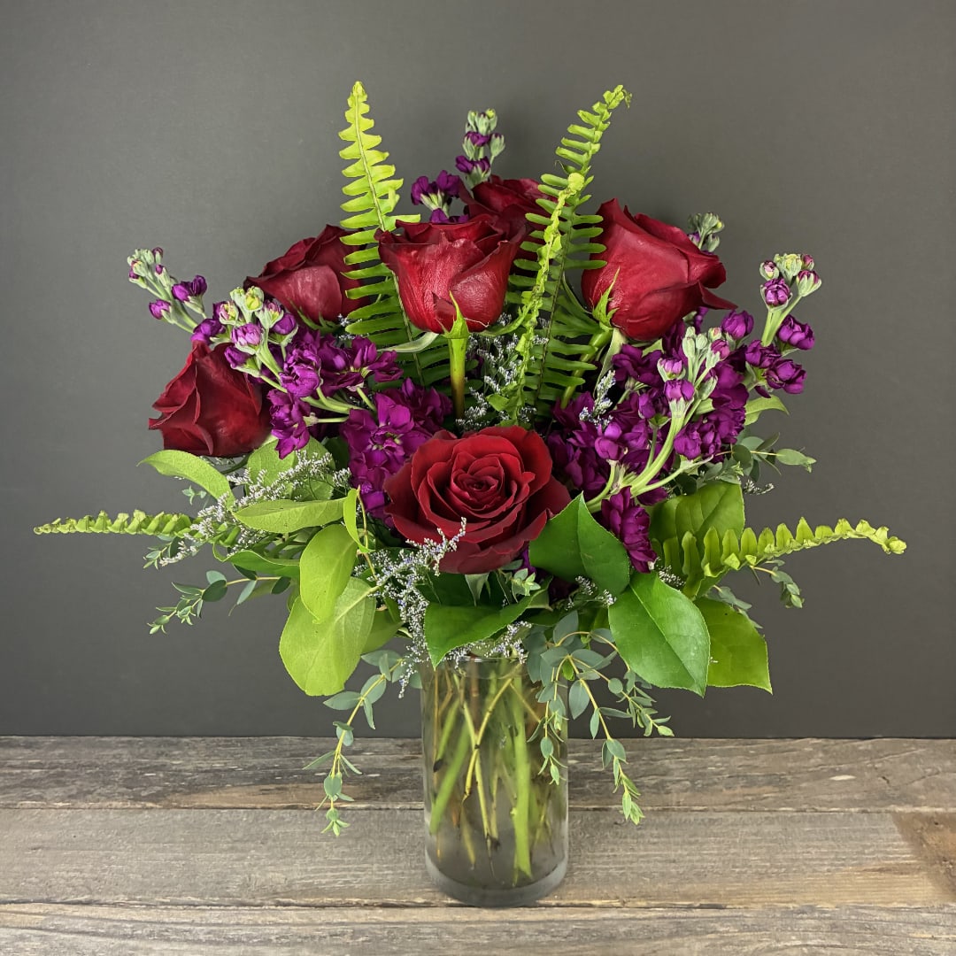 Bouquet of red roses and purple flowers in a clear glass vase