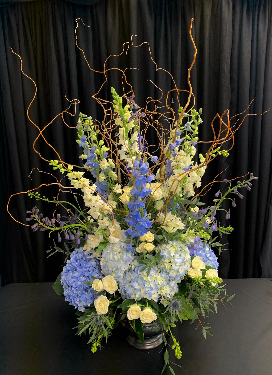 Tall blue and white floral arrangement in a black vase with curly branches
