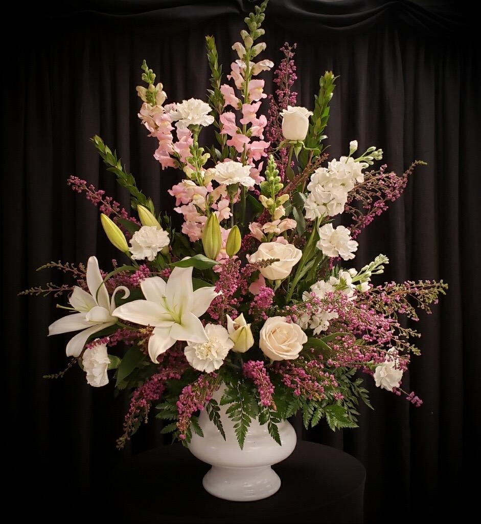 Tall floral arrangement with white lilies, roses, and pink blooms in a white vase
