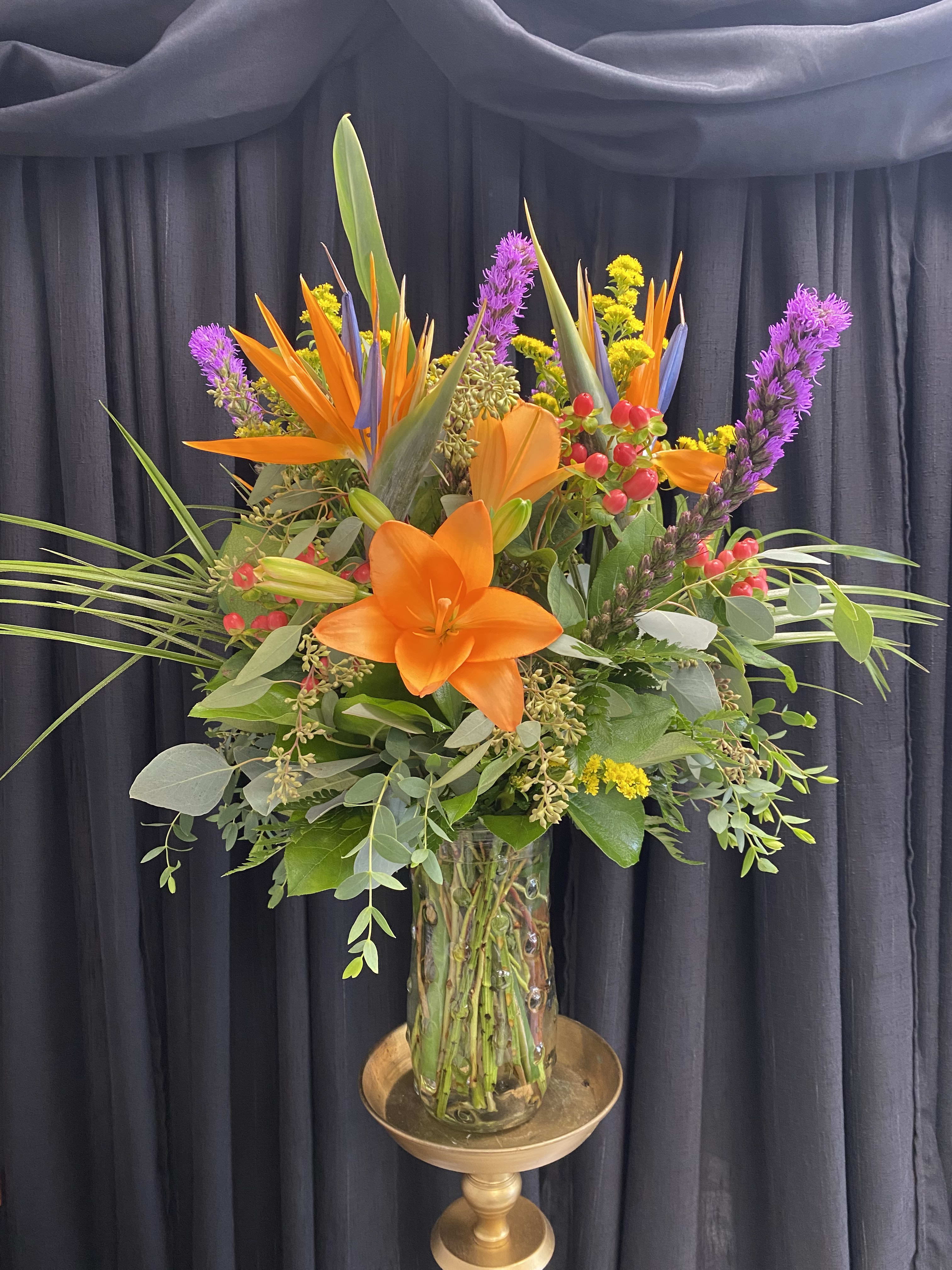 Tall tropical bouquet with orange lilies in a glass vase