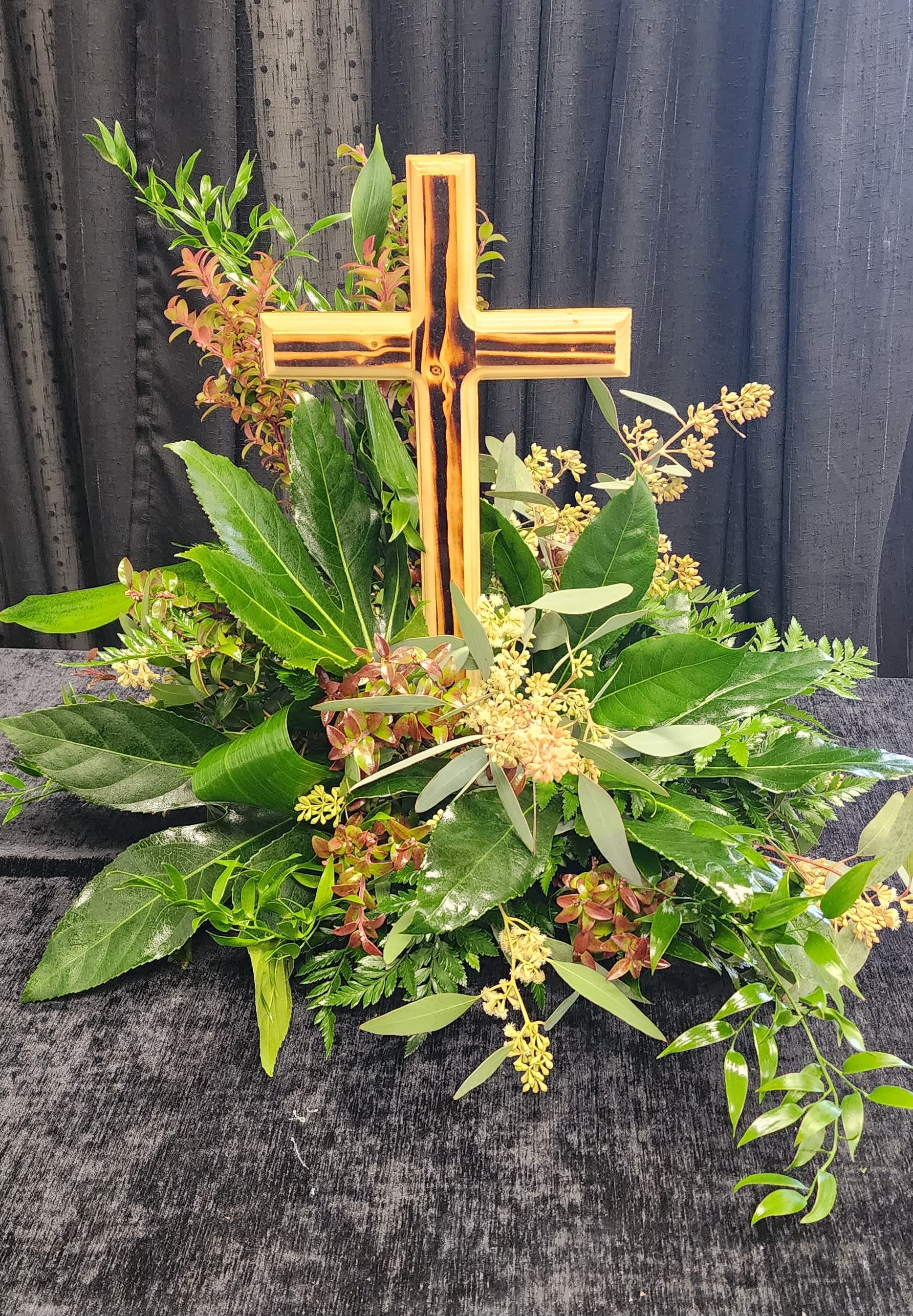 Cross-shaped floral tribute with mixed greenery and small pale blooms
