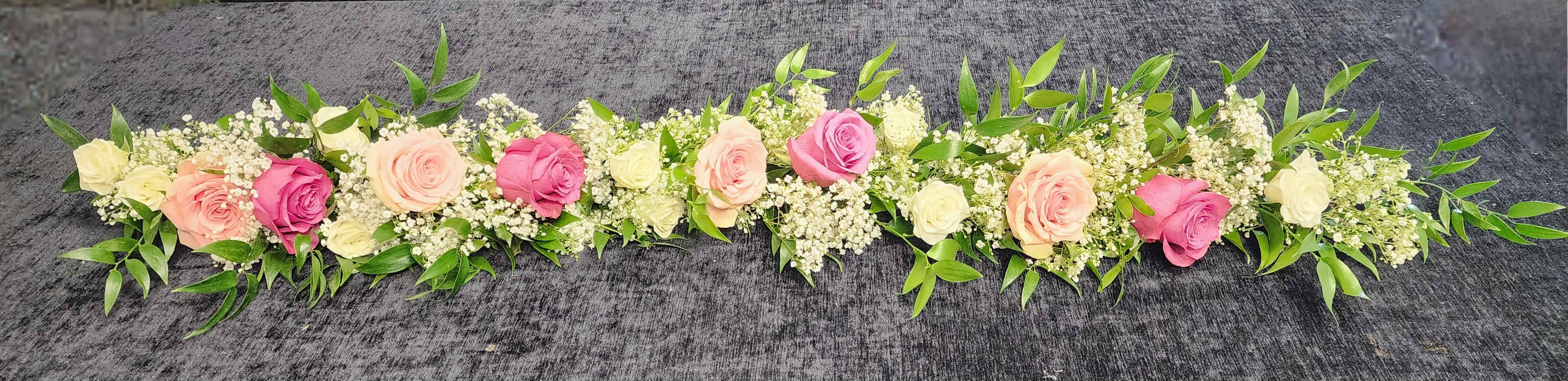 Long floral garland with pink and cream roses on a dark surface