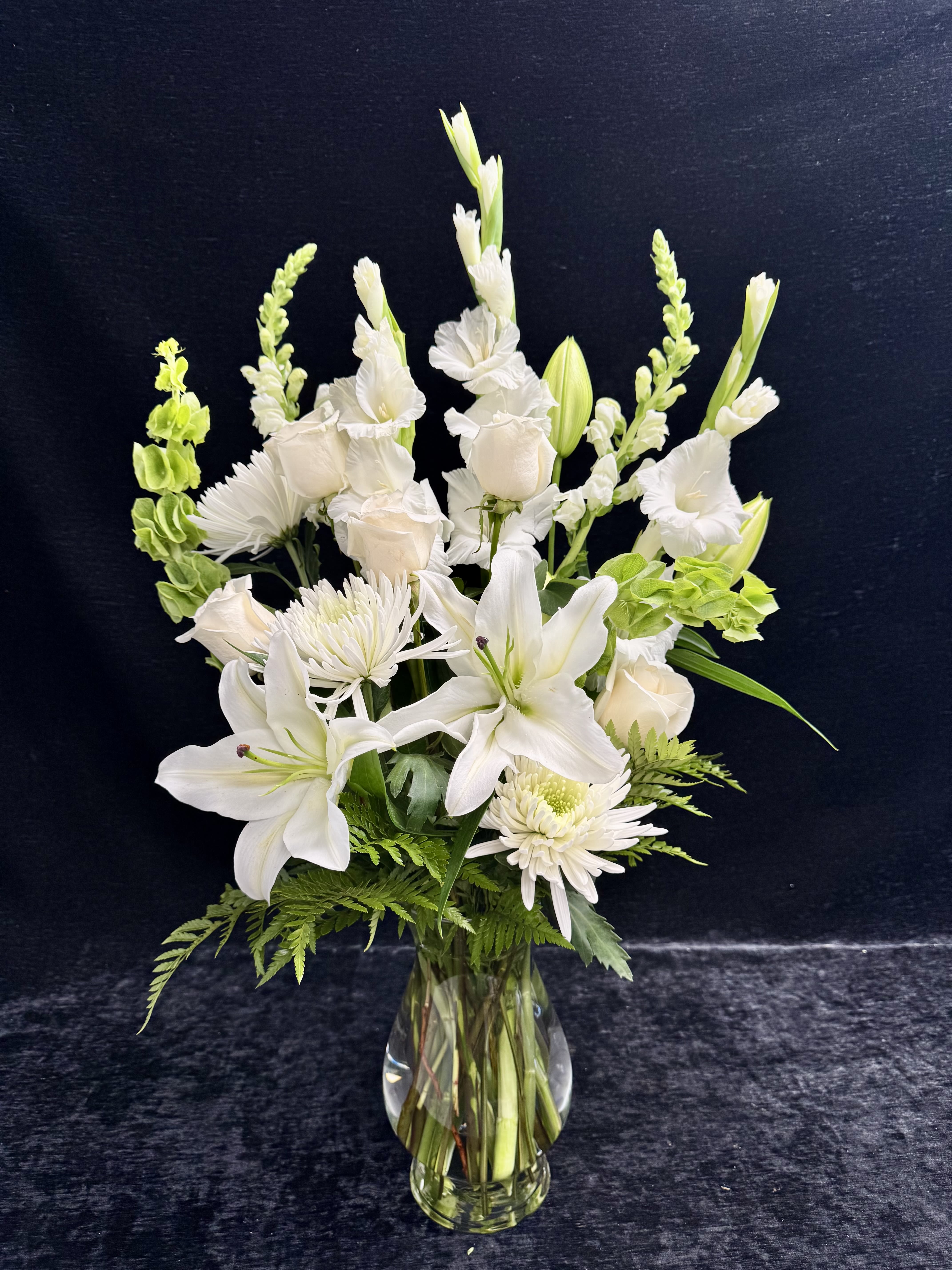 White lilies and roses arranged in a clear glass vase with green accents.