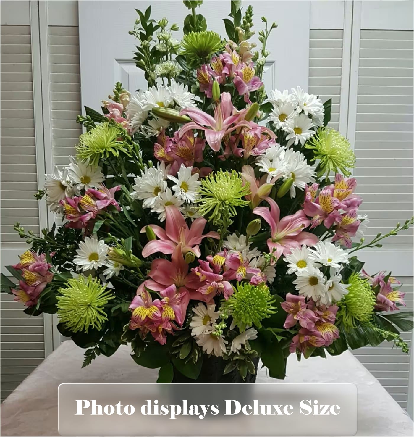 Tall arrangement of pink lilies, white daisies, and green mums in a dark vase