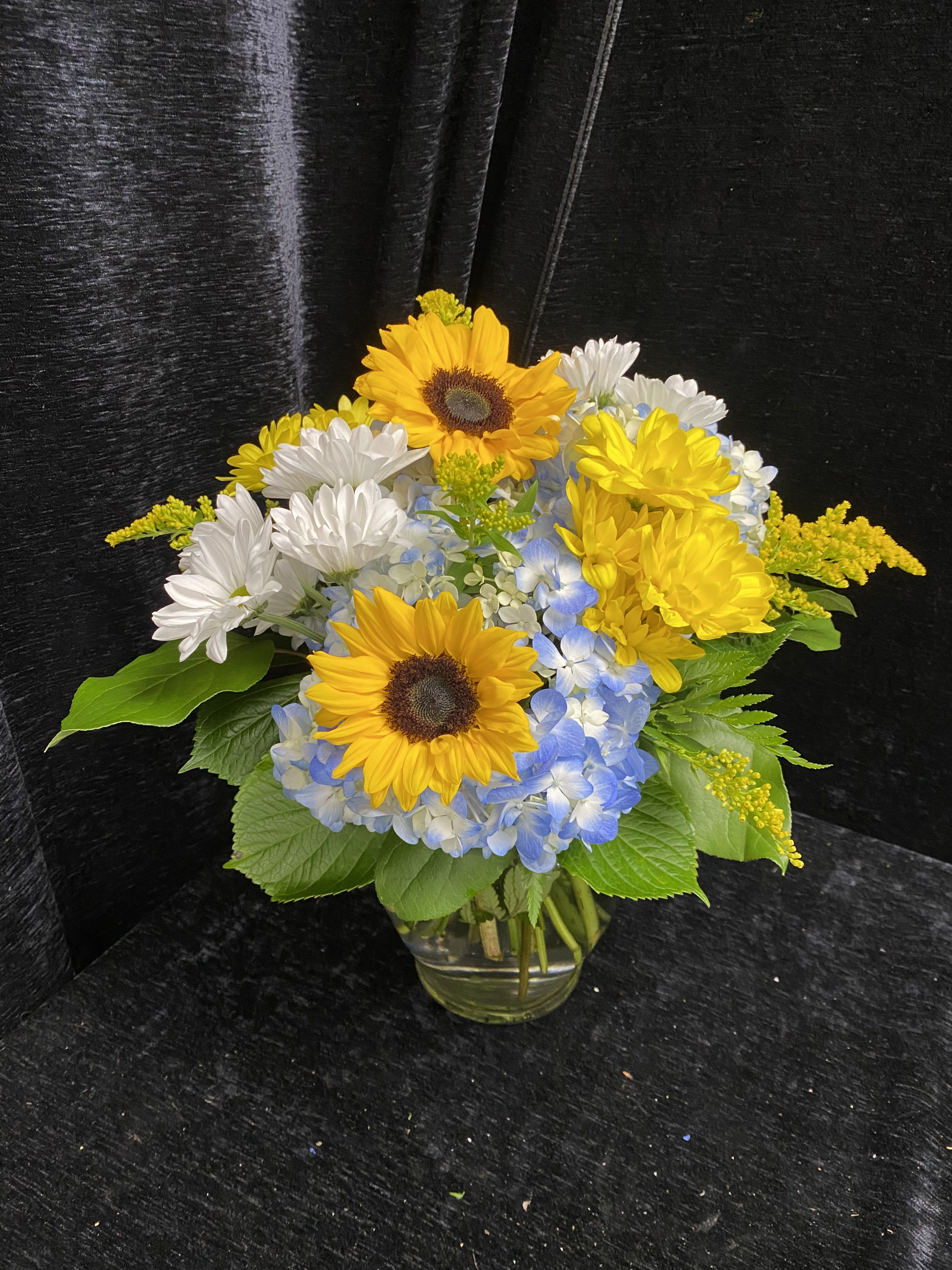 Sunny Blue Skies - Brighten someone's day. Arrangement with blue hydrangea, sunflowers, daisies and solidago in a low ginger jar