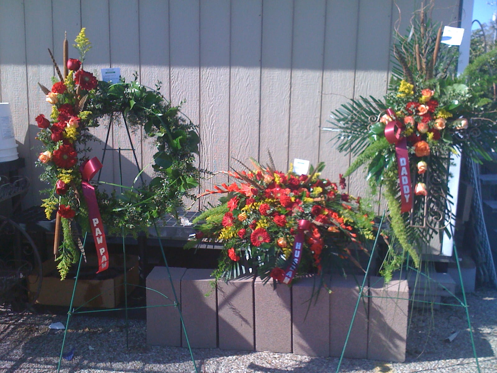 Three standing funeral wreaths with red and orange flowers on easels