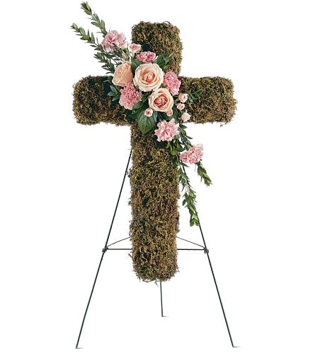 Moss-covered cross with pink and peach flowers on a stand