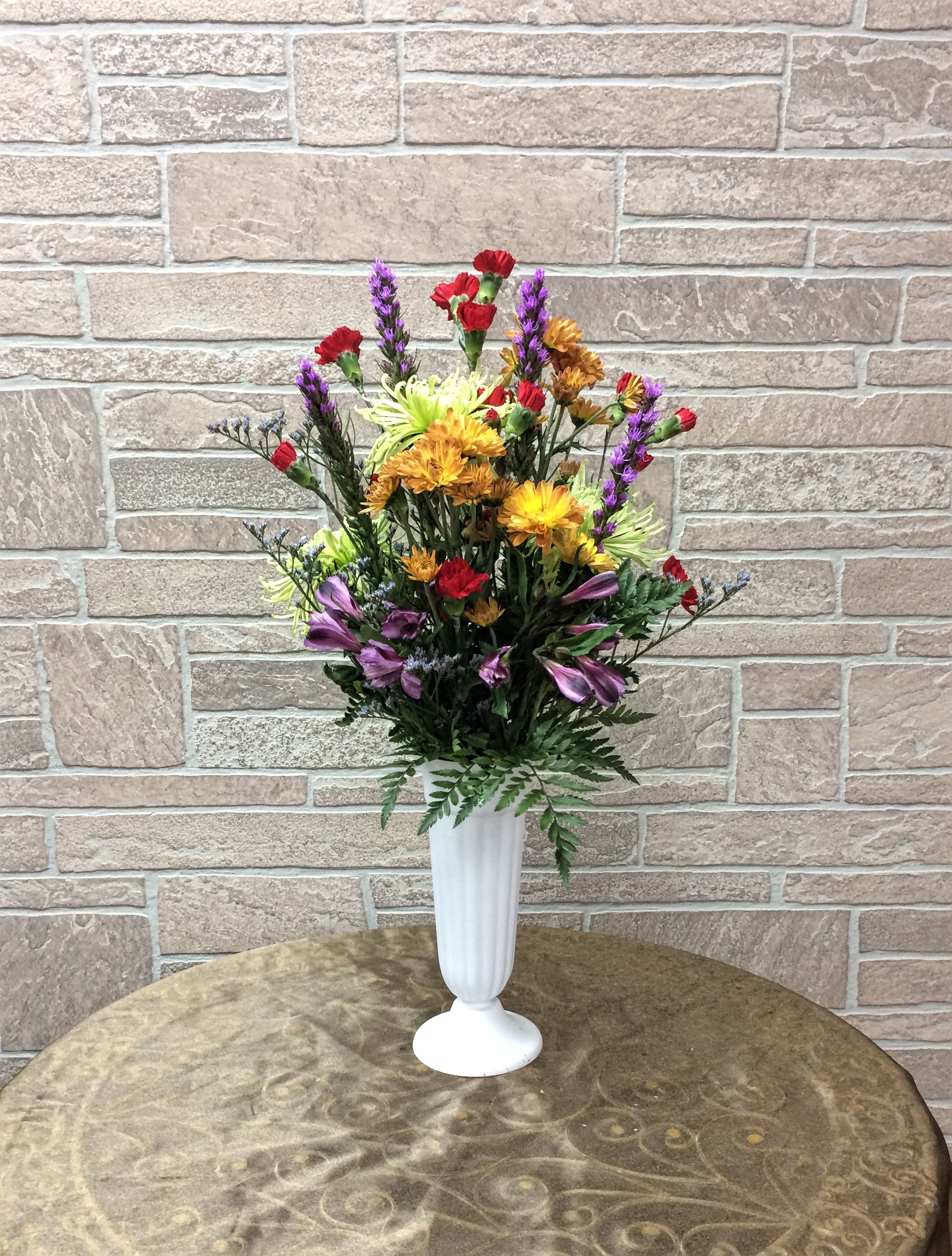 Mixed bouquet in a white pedestal vase with red, purple, and yellow flowers