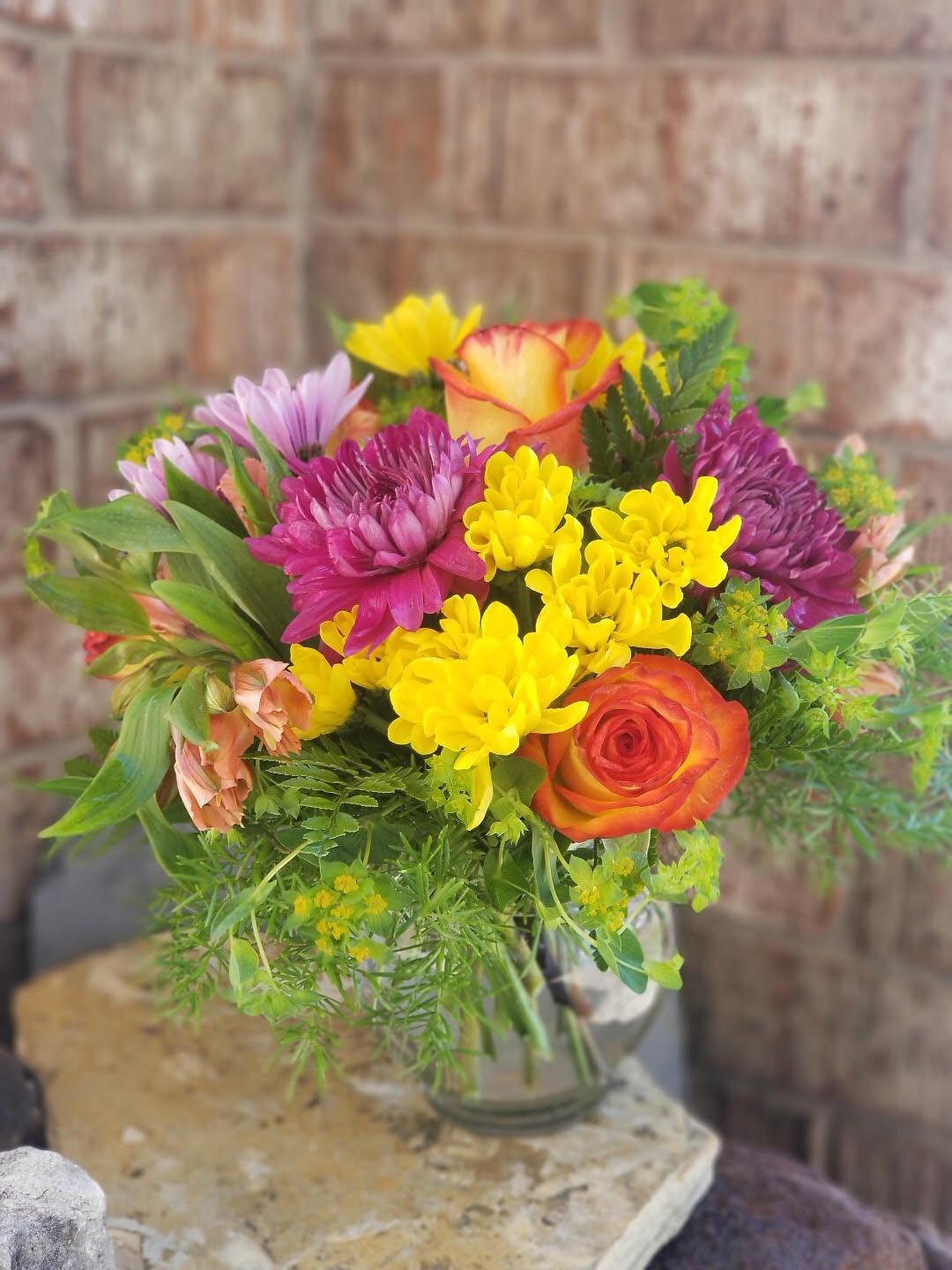 Mixed bouquet of yellow, purple, and orange flowers in a glass vase