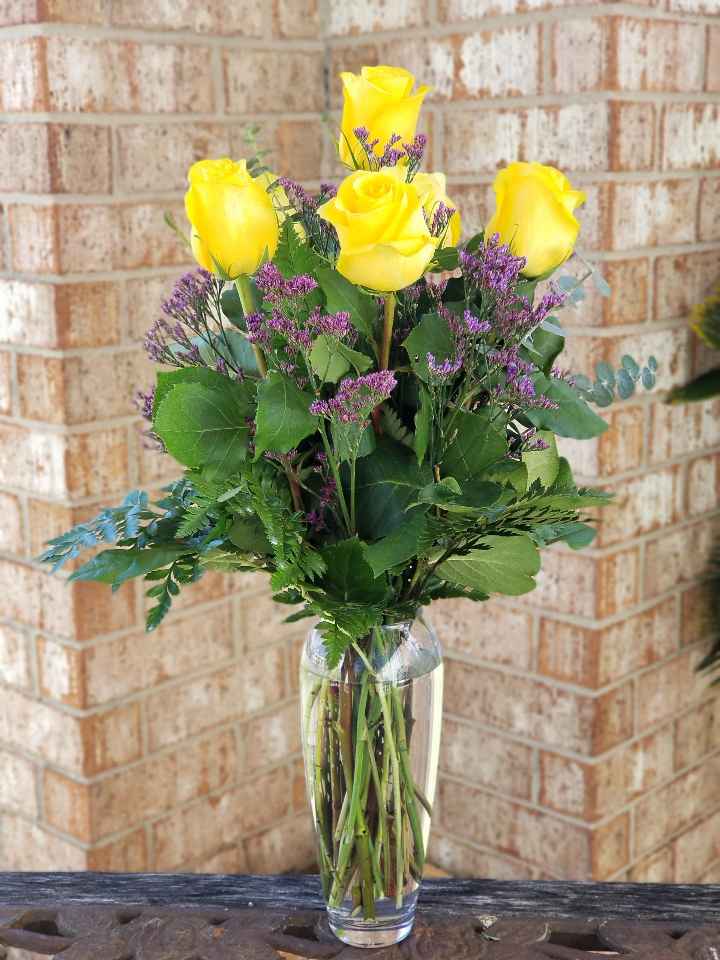 Yellow roses with purple filler in a clear glass vase