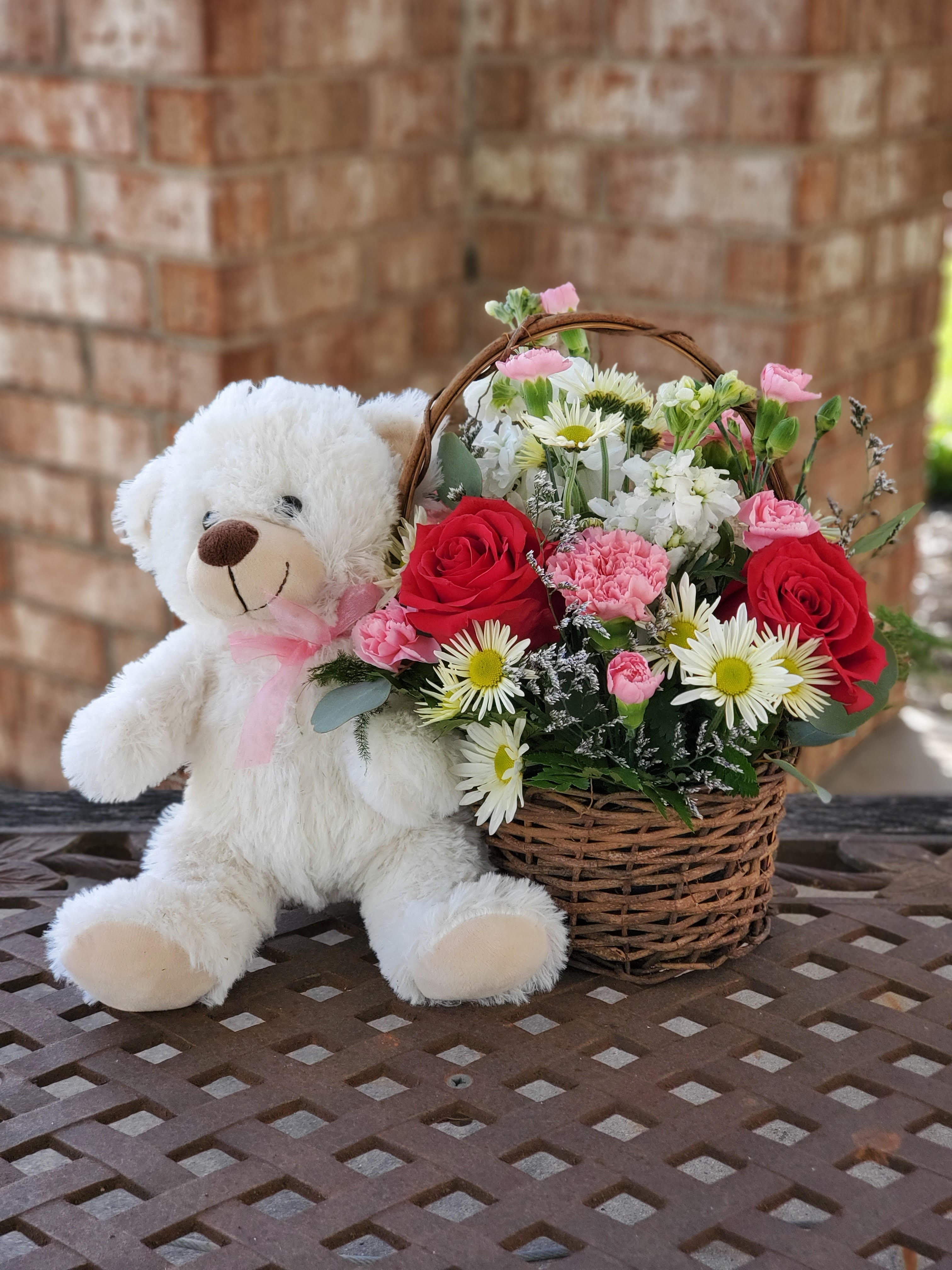 White teddy bear beside a basket of red and pink flowers