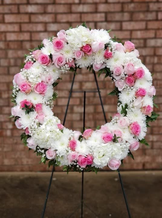 Pink and white floral wreath on a black stand