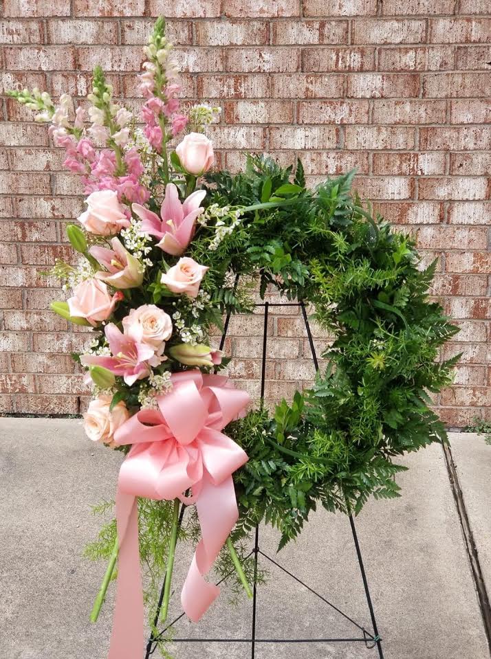 Pink and white floral wreath on a stand with a large pink bow
