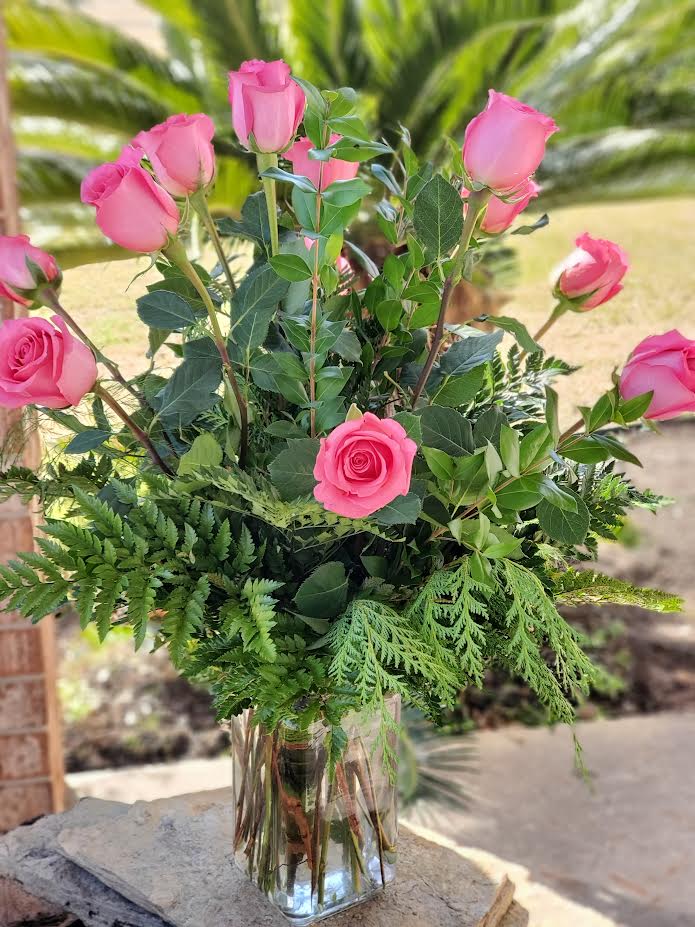 Tall arrangement of pink roses with lush greenery in a clear glass vase