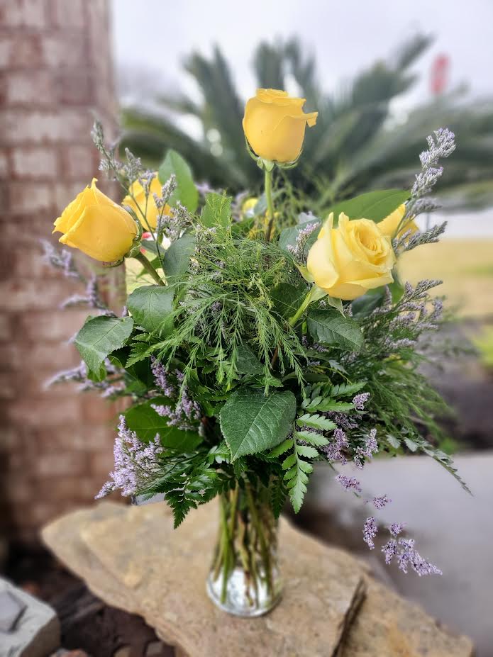 Yellow roses in a clear glass vase with mixed greenery