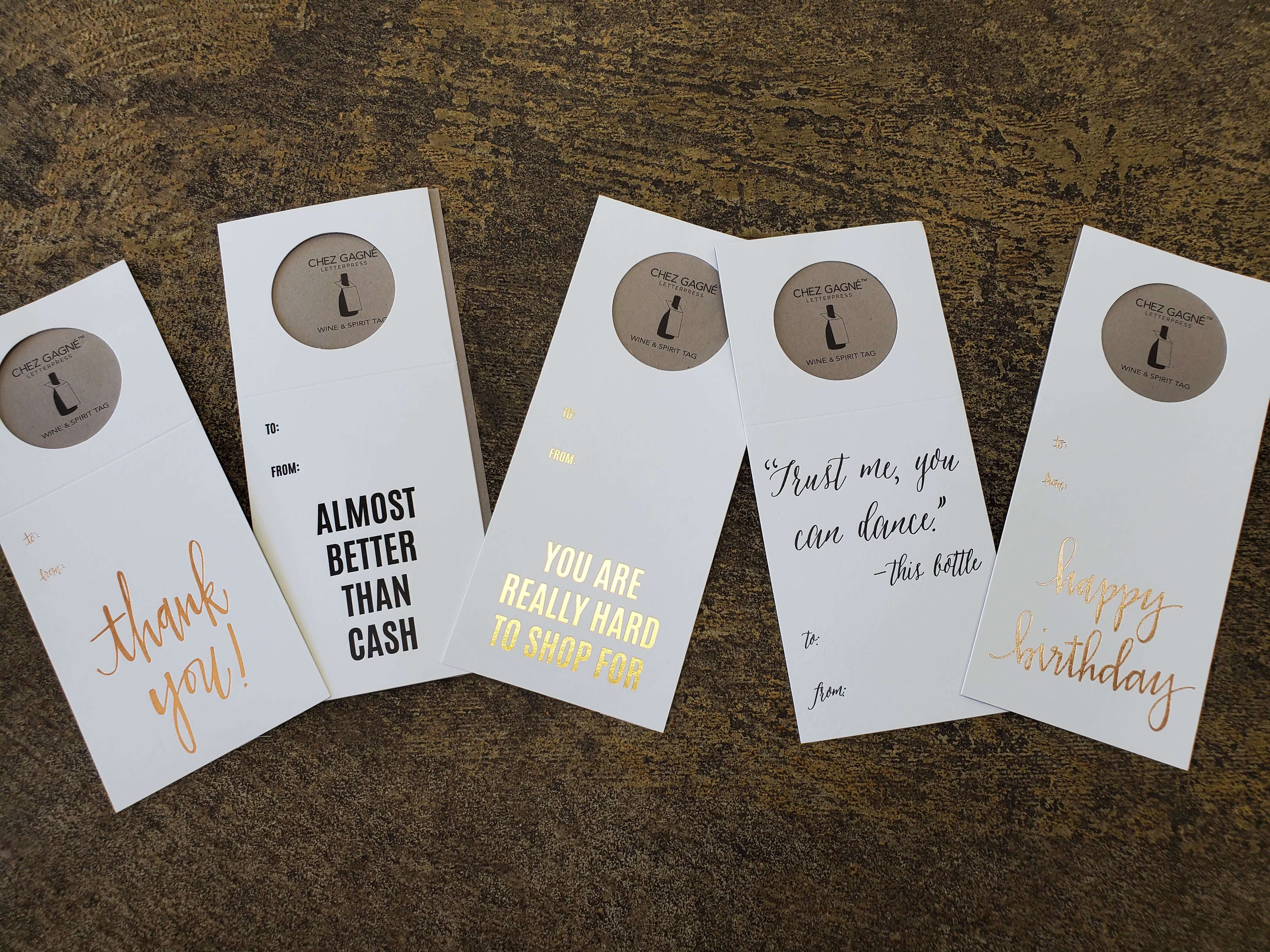 Five greeting card sleeves with gold and black text on a textured surface.