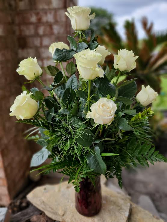 White roses arranged in a tall vase with dense greenery