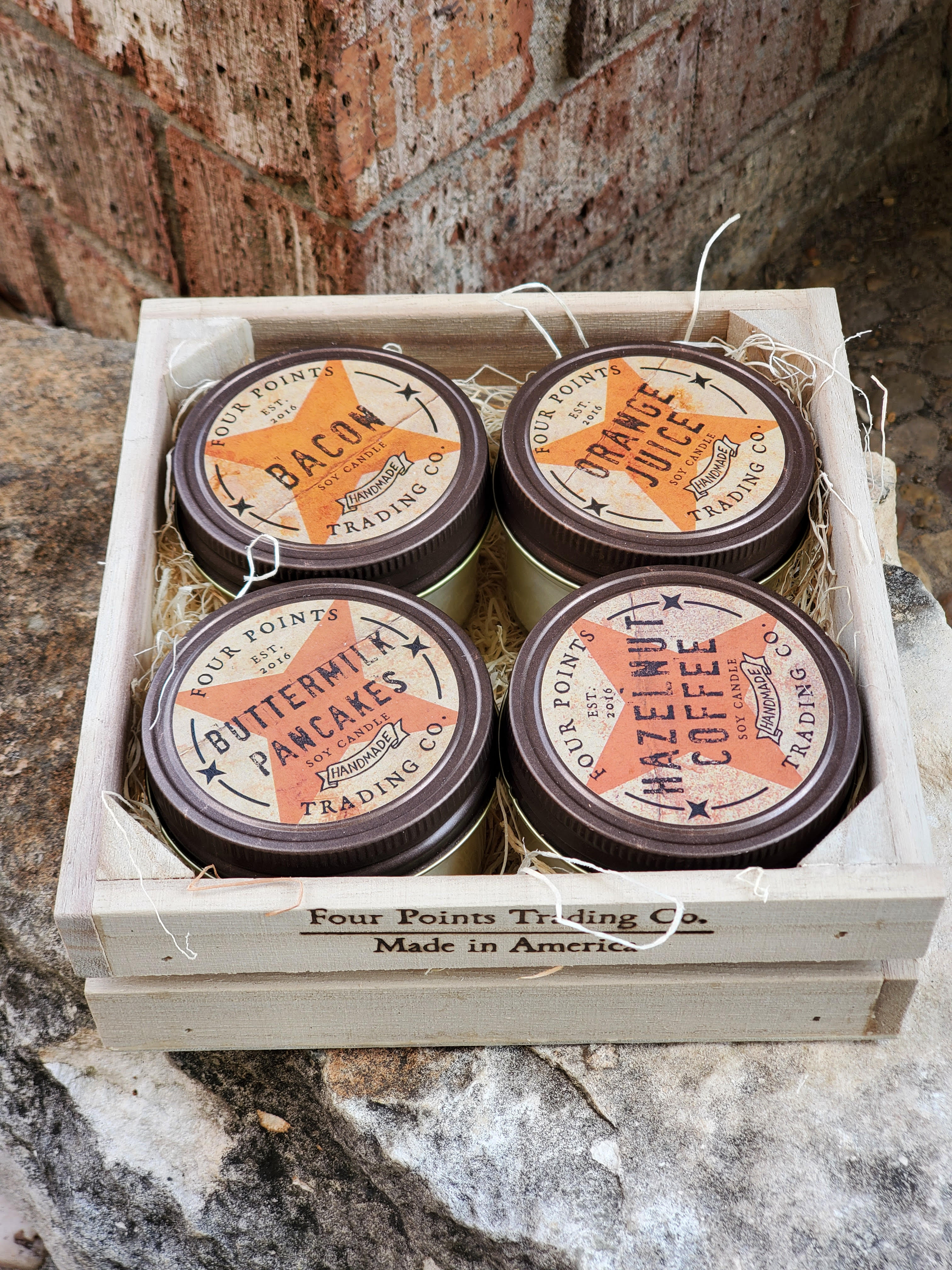 Four scented candles in a wooden crate with straw filler