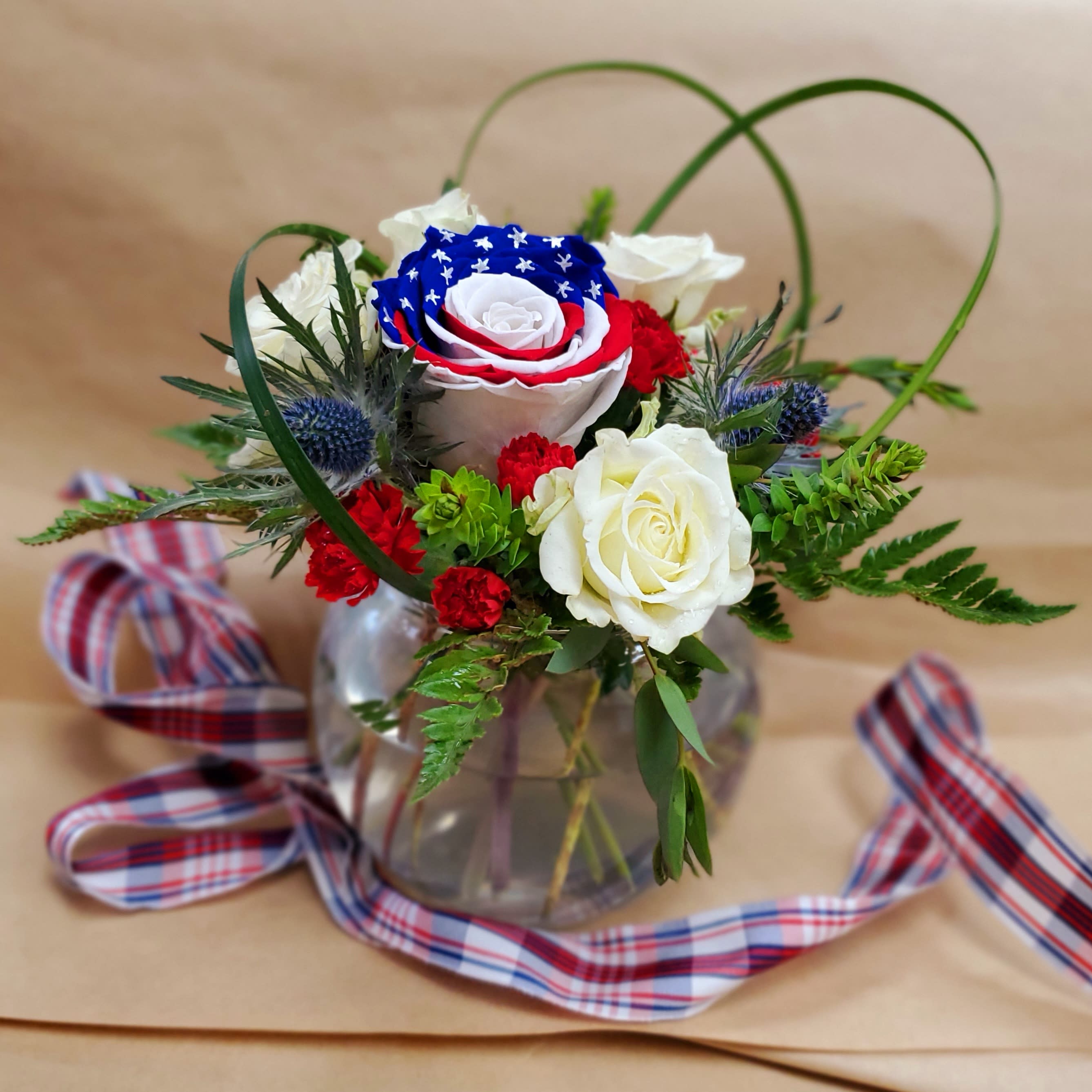 Red, white, and blue rose arrangement in a glass vase with plaid ribbon