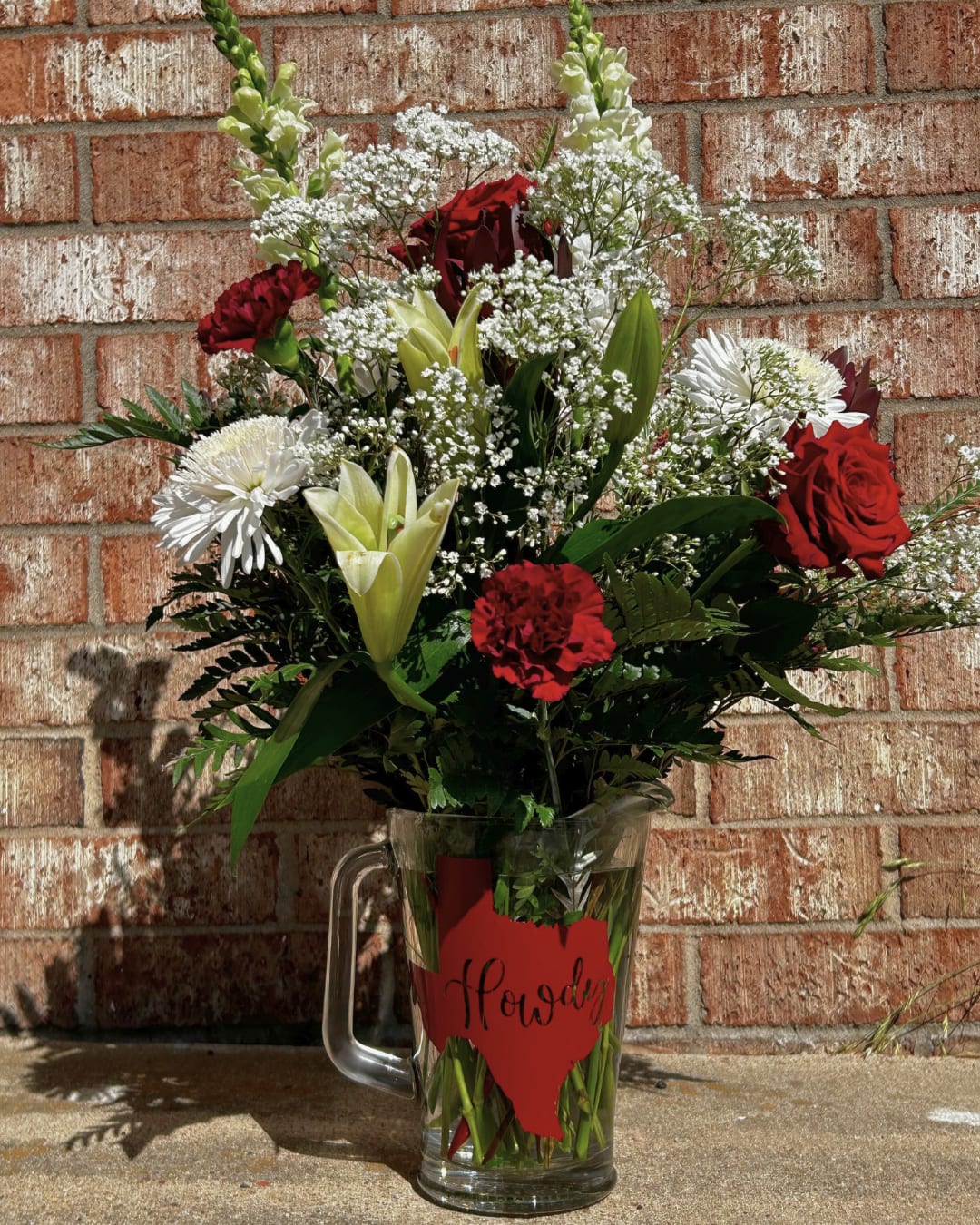 Red and white mixed flower arrangement in a glass pitcher