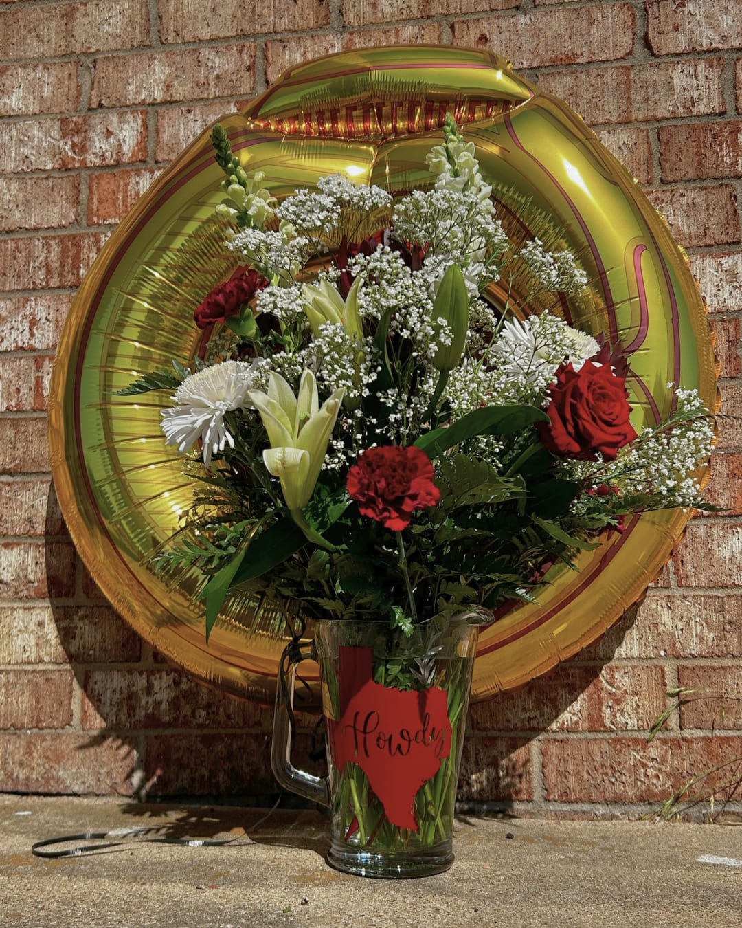 Bouquet of red and white flowers in a glass mug with a gold balloon behind it