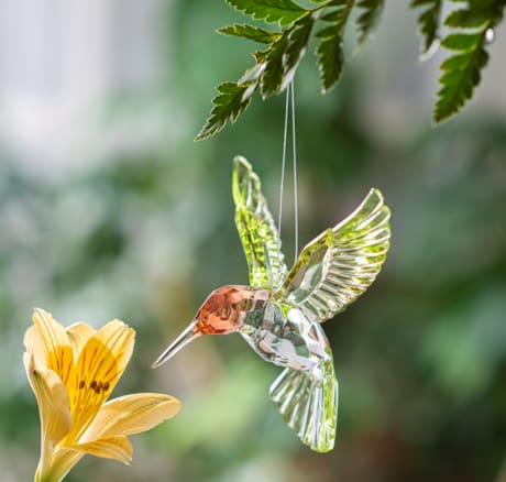 Glass hummingbird ornament hanging near a yellow flower