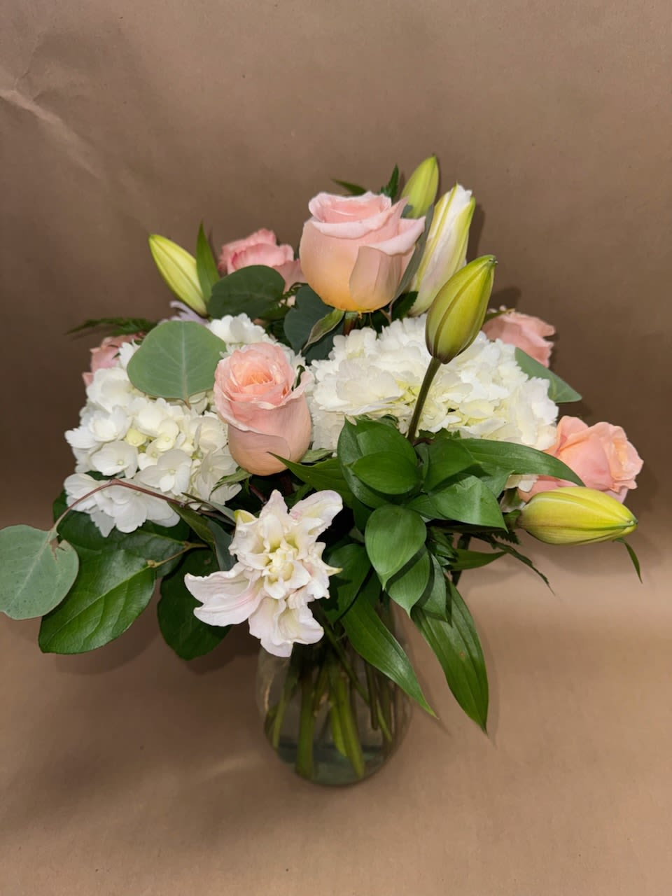 Pink roses and white hydrangeas in a glass vase with lily buds