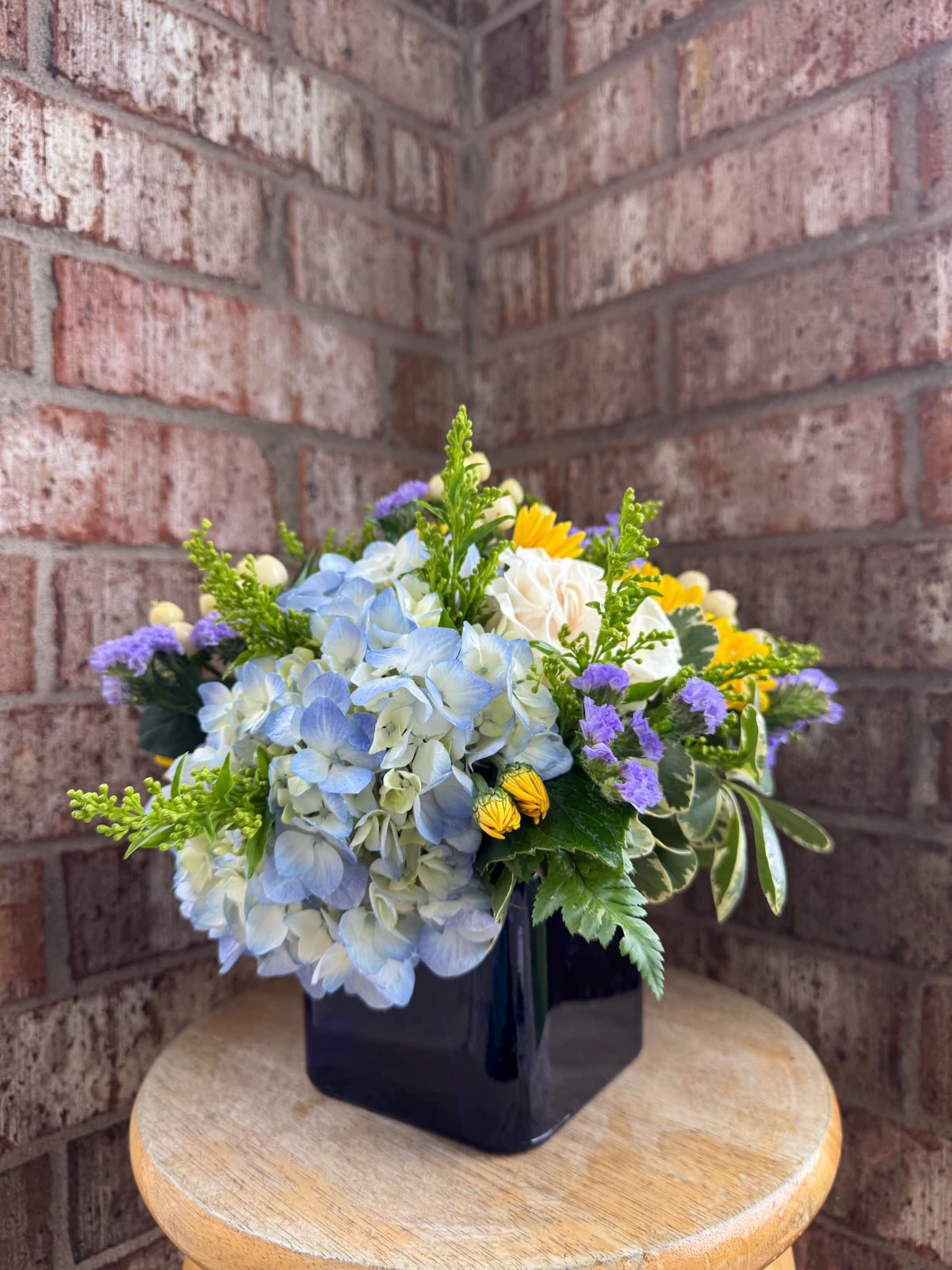 Blue hydrangea bouquet in a black square vase with yellow and purple accents
