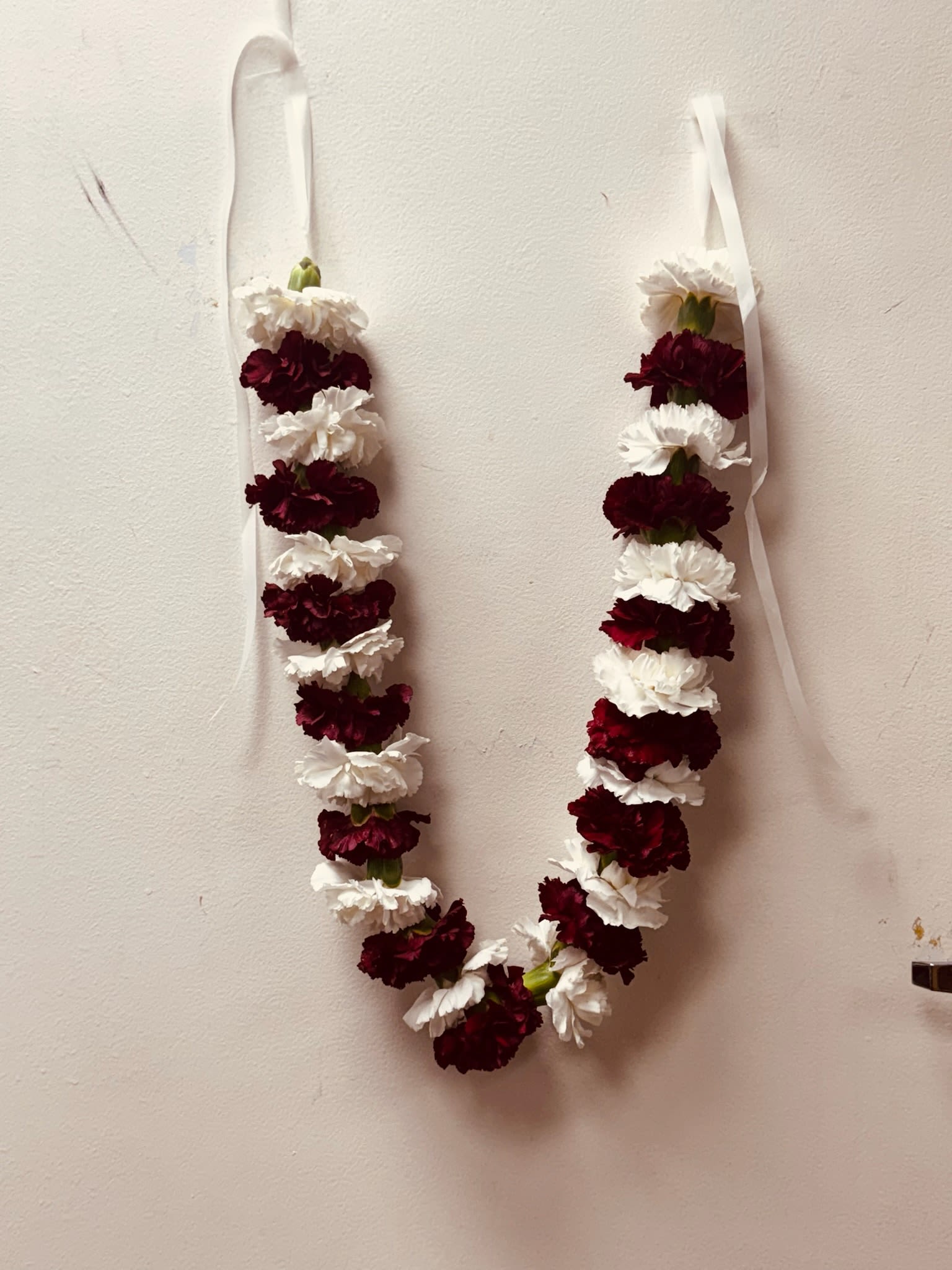 Two white and burgundy flower garlands hang on a wall.