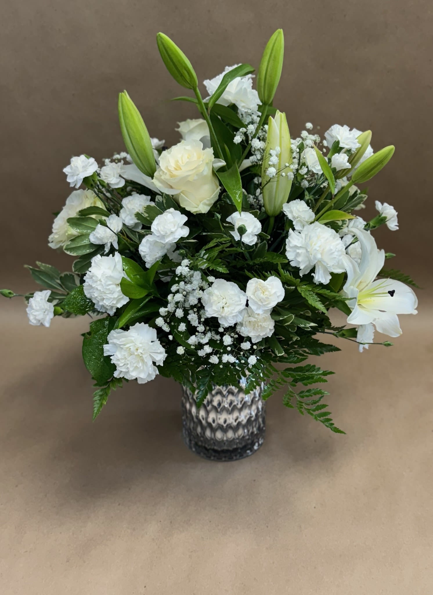 White floral arrangement with lilies, roses, and carnations in a patterned vase