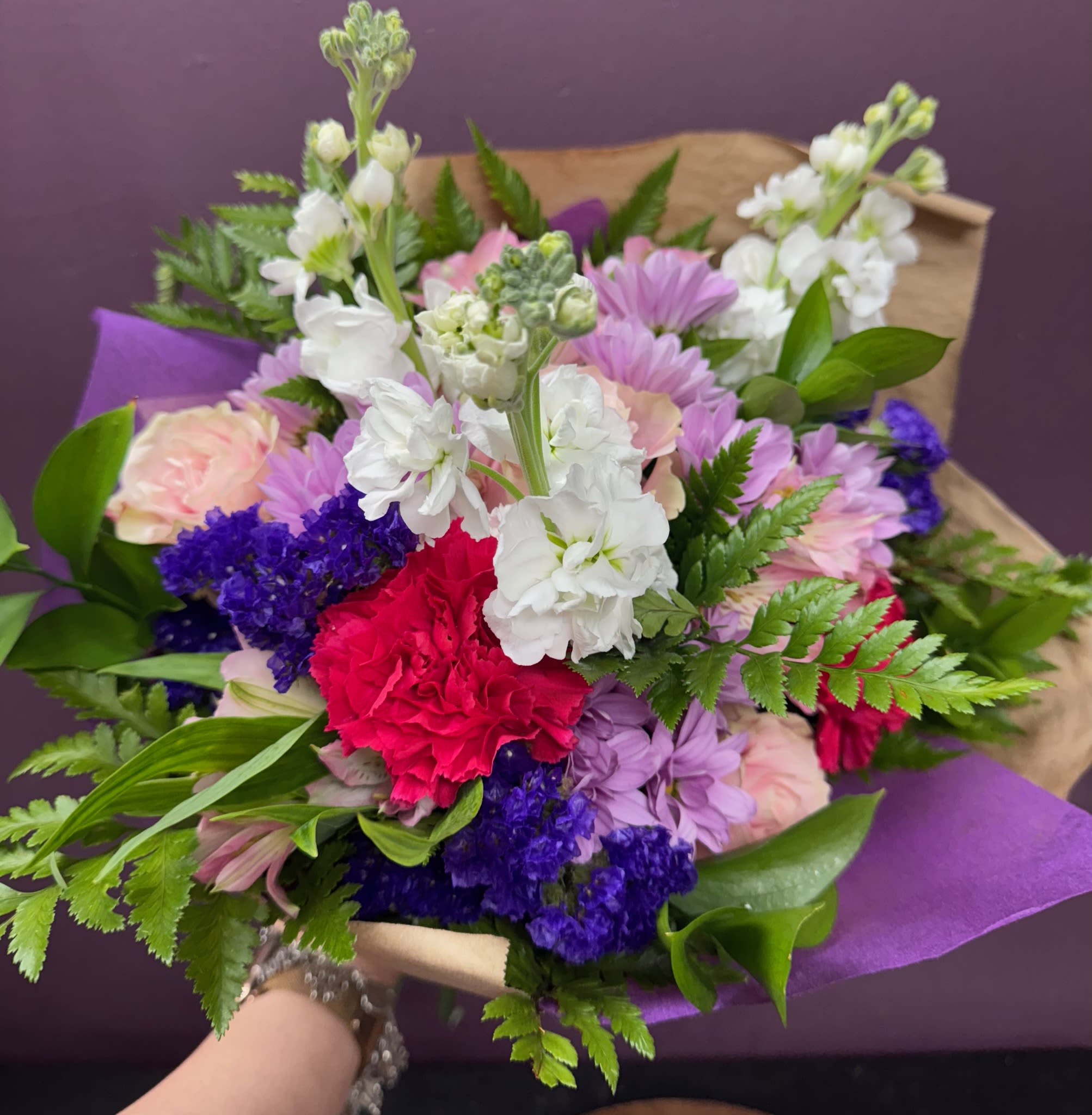 Mixed bouquet of pink, white, purple, and red flowers wrapped in purple paper