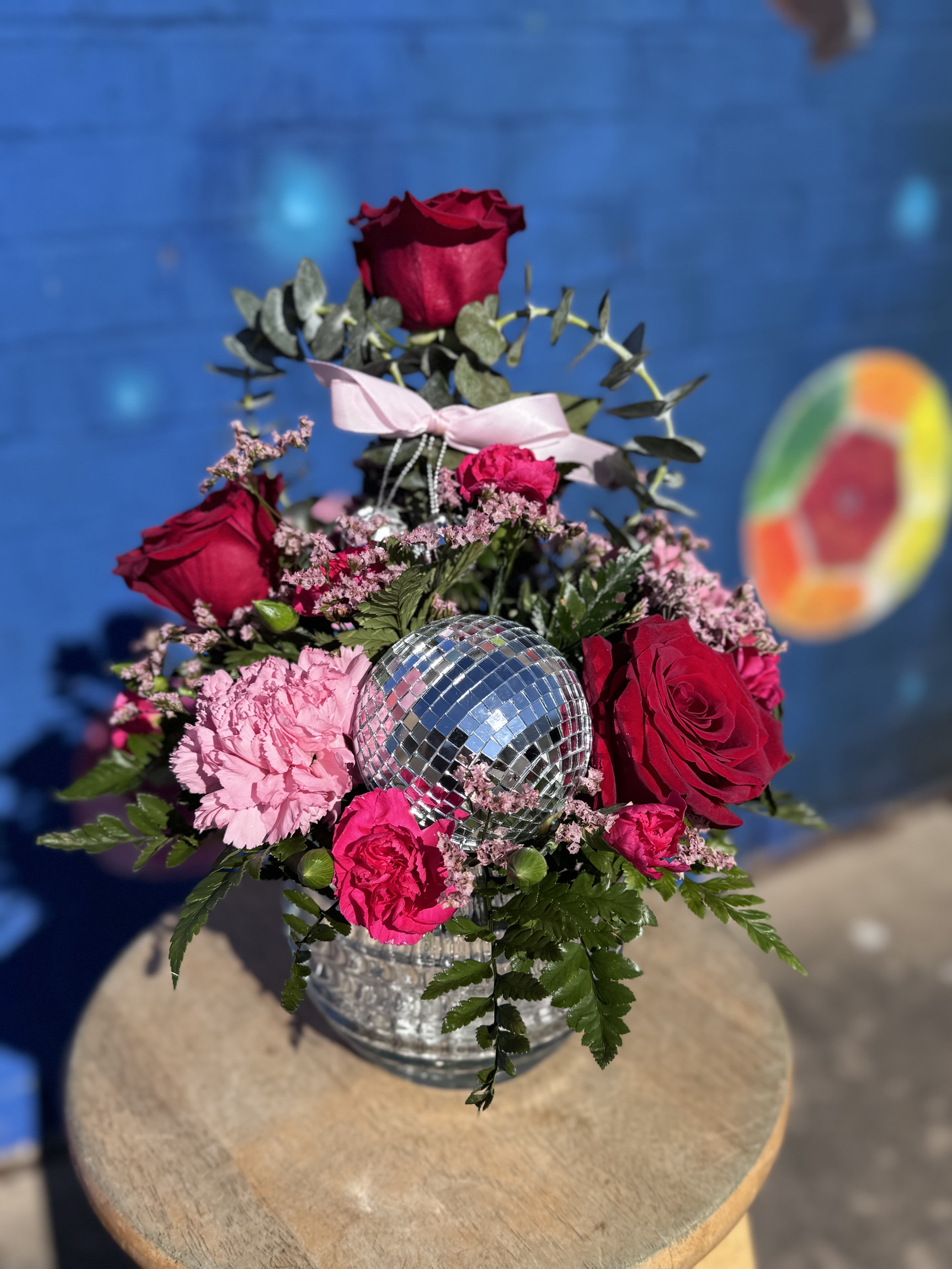 Pink and red roses arranged around a mirrored disco ball in a glass vase