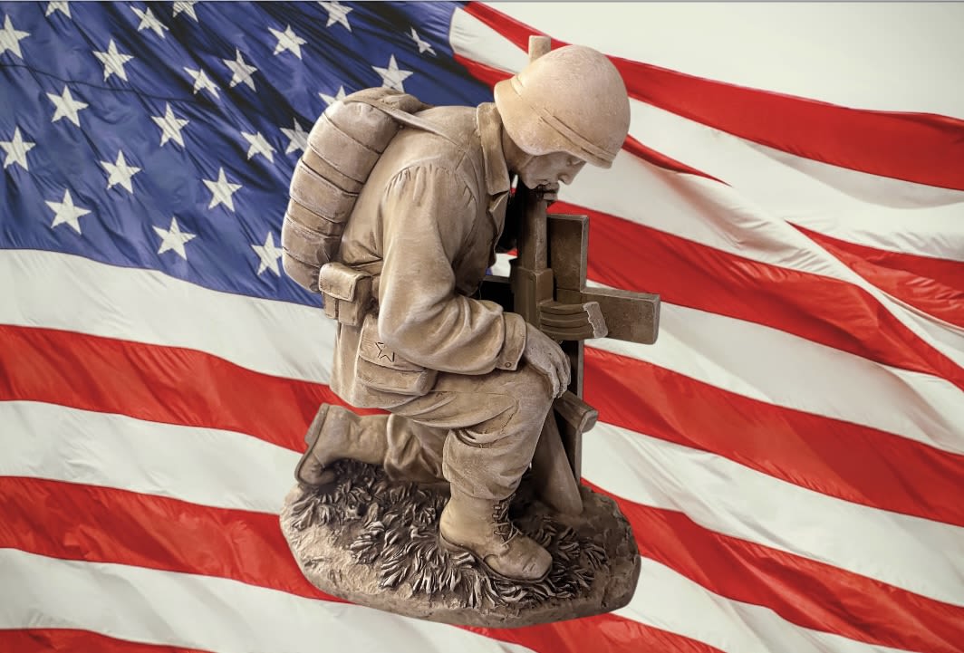 A kneeling soldier statue in front of an American flag.
