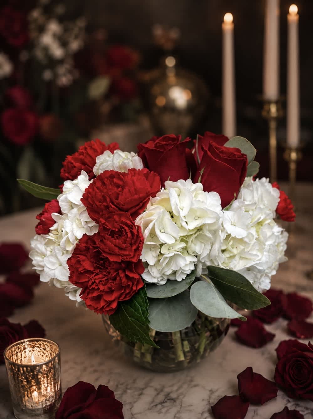 Red roses and white carnations in a glass vase with candles