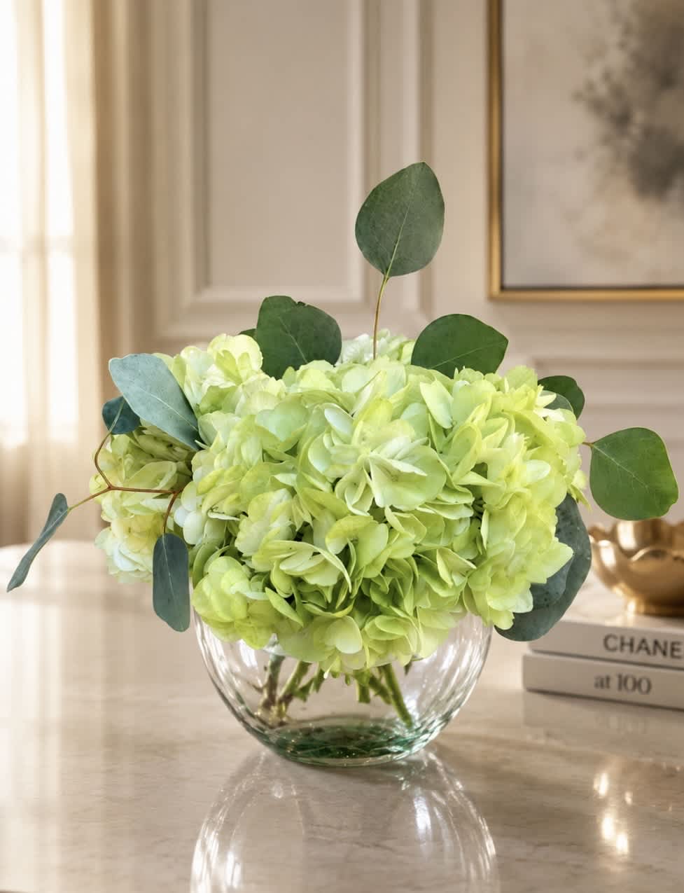 Lime green hydrangeas in a clear glass bowl vase with eucalyptus