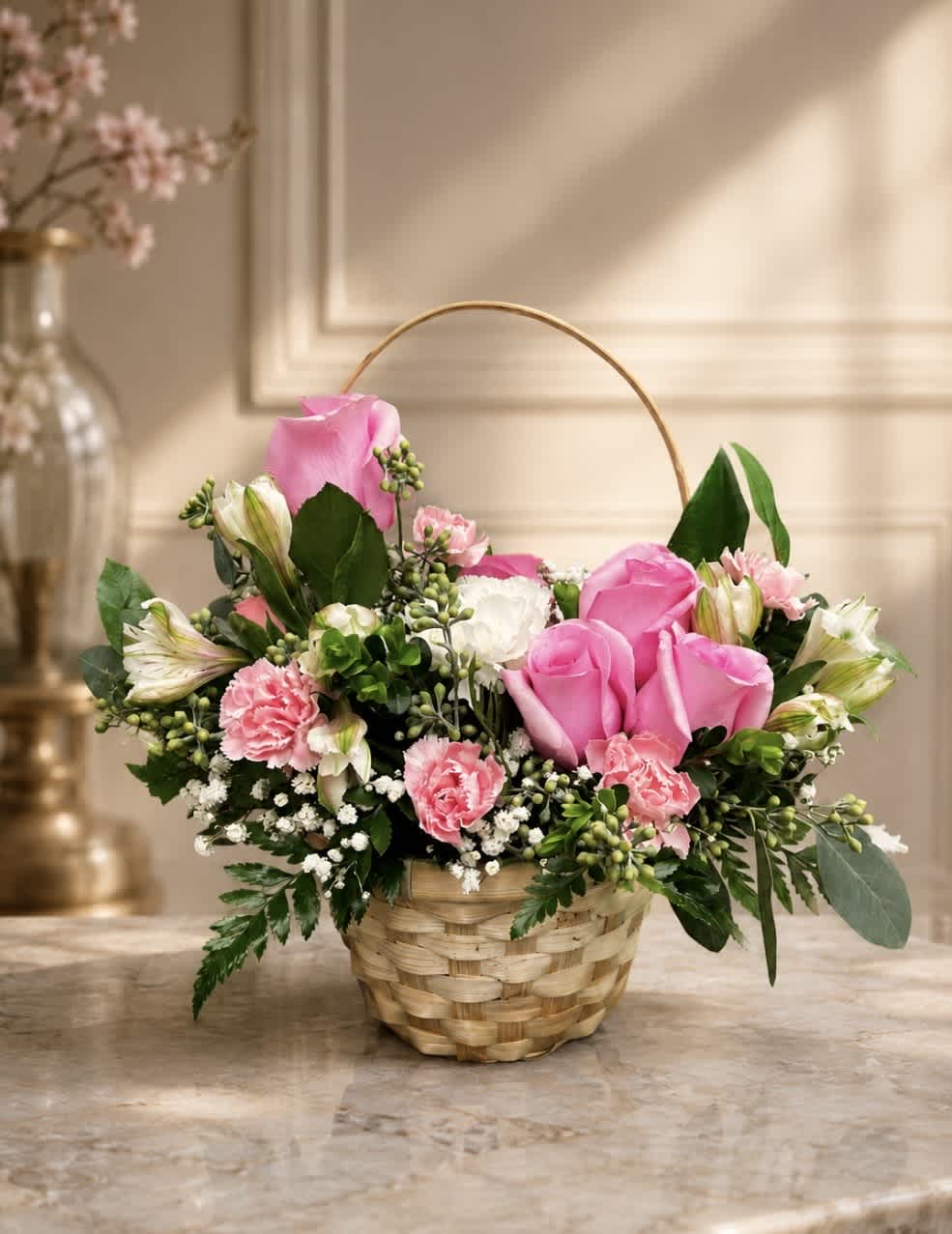 Pink roses and carnations arranged in a wicker basket with a handle