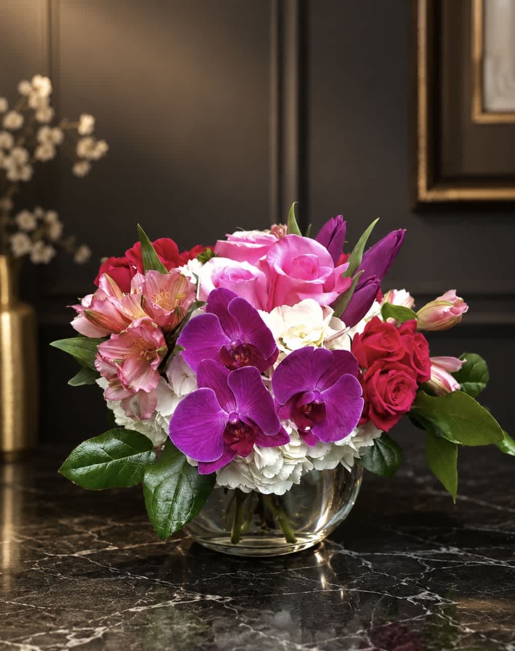 Mixed bouquet of pink roses, purple orchids, and white blooms in a glass bowl vase