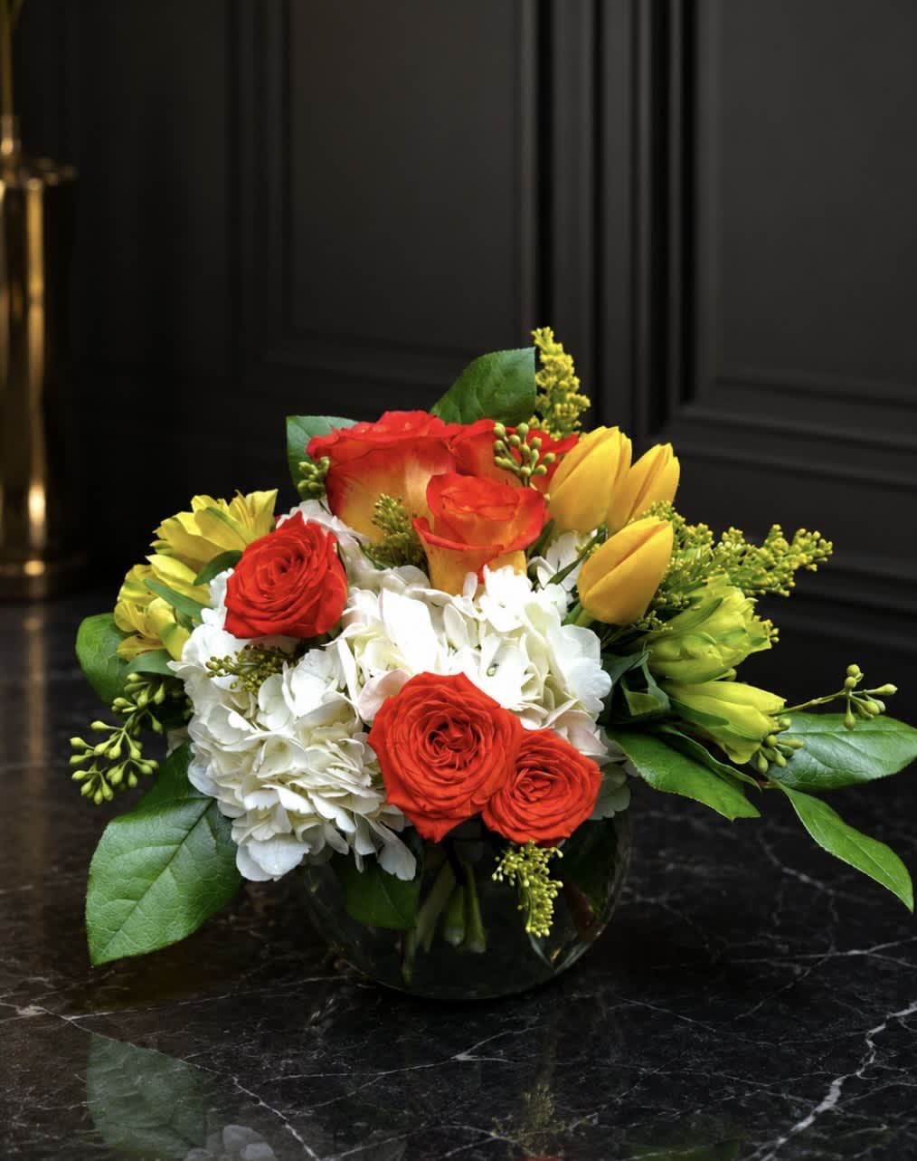 Bouquet of red roses, white hydrangeas, and yellow tulips in a glass vase
