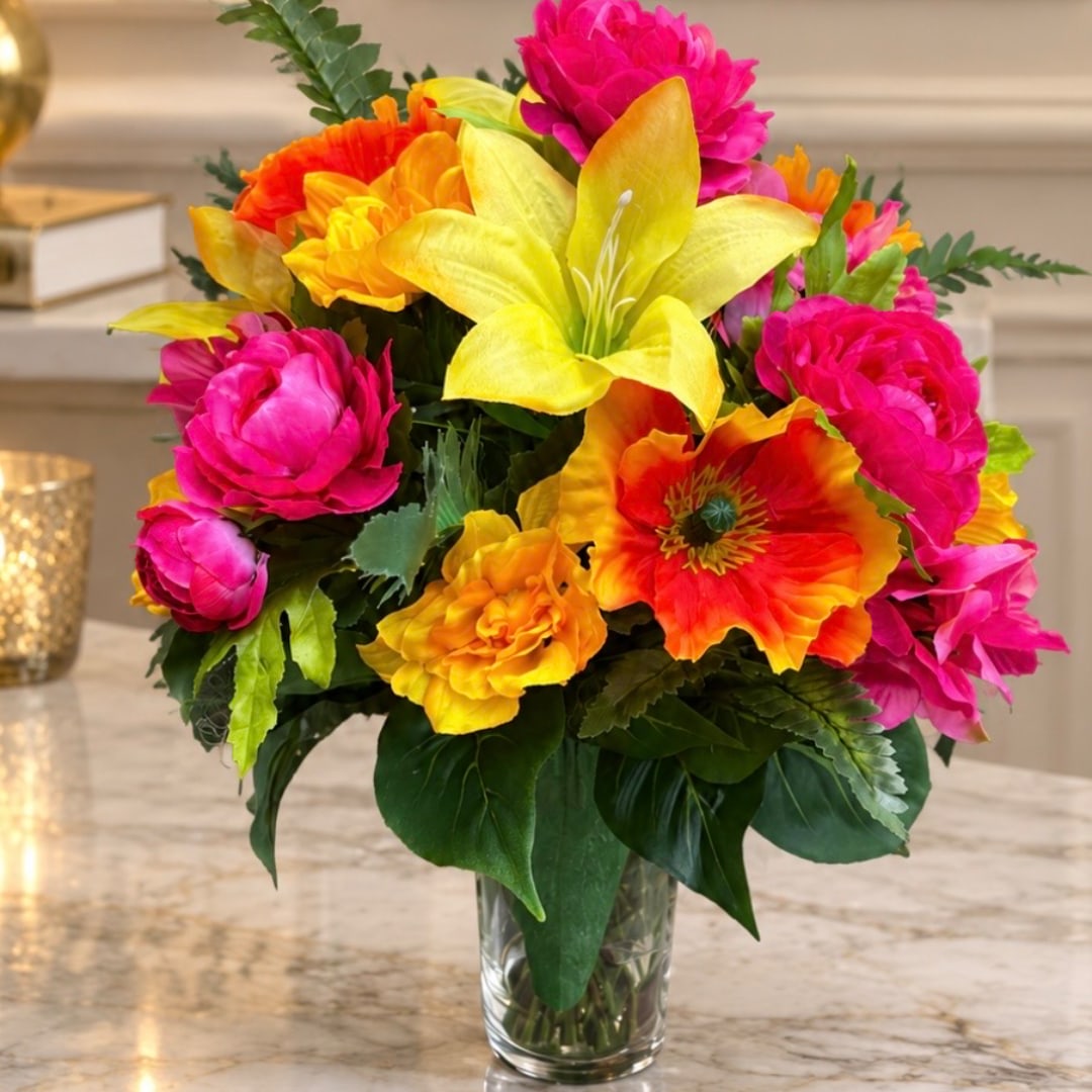 Bright mixed bouquet of pink, yellow, and orange flowers in a clear glass vase.