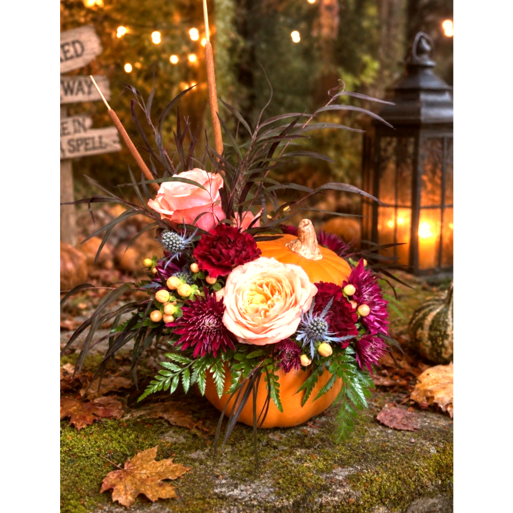Floral arrangement in a pumpkin container with roses and dark mums