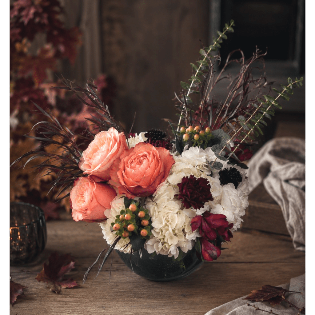 Coral roses and white hydrangeas in a dark vase with burgundy accents