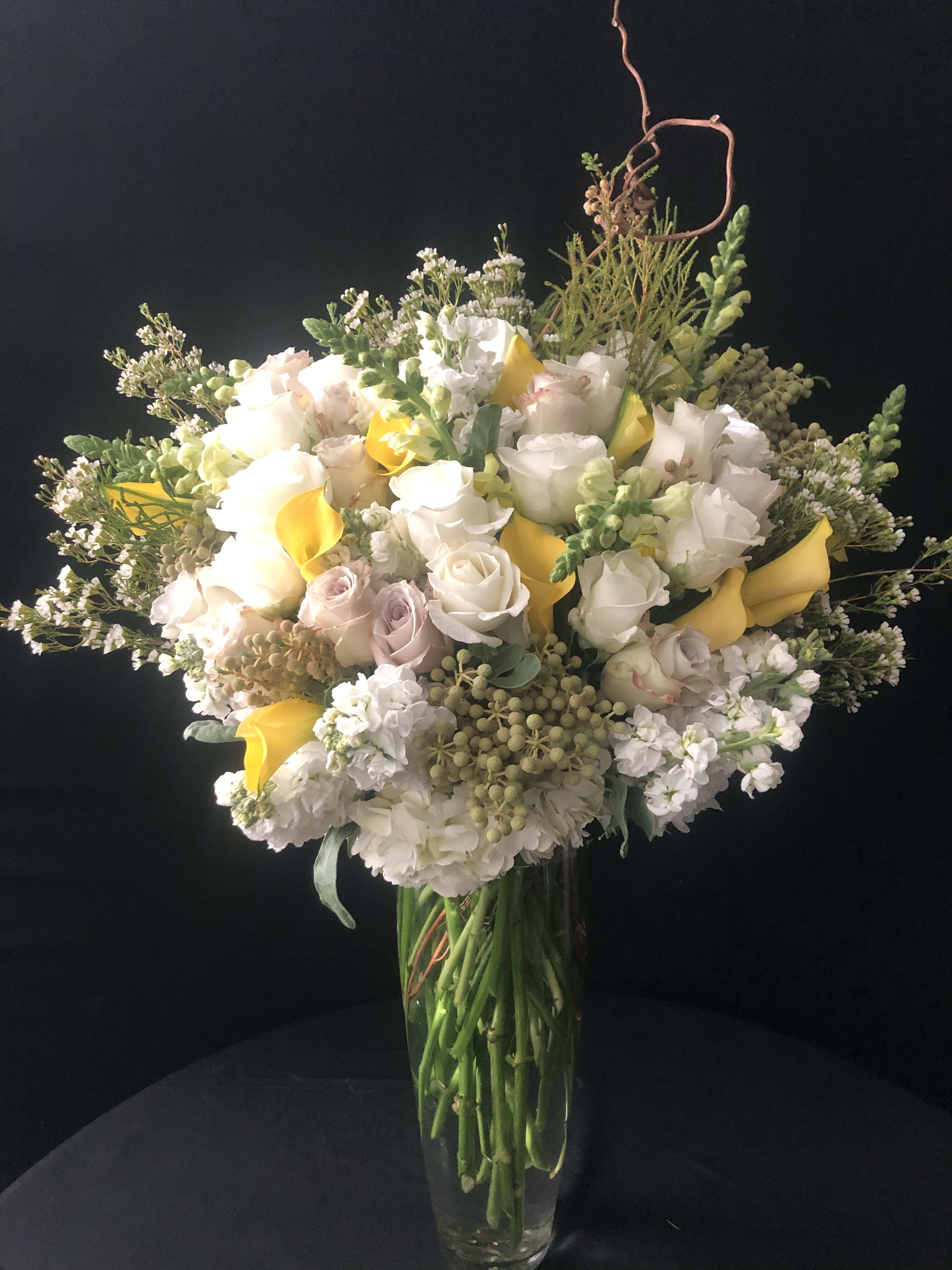 Bouquet of white and pale pink roses with yellow calla lilies in a glass vase