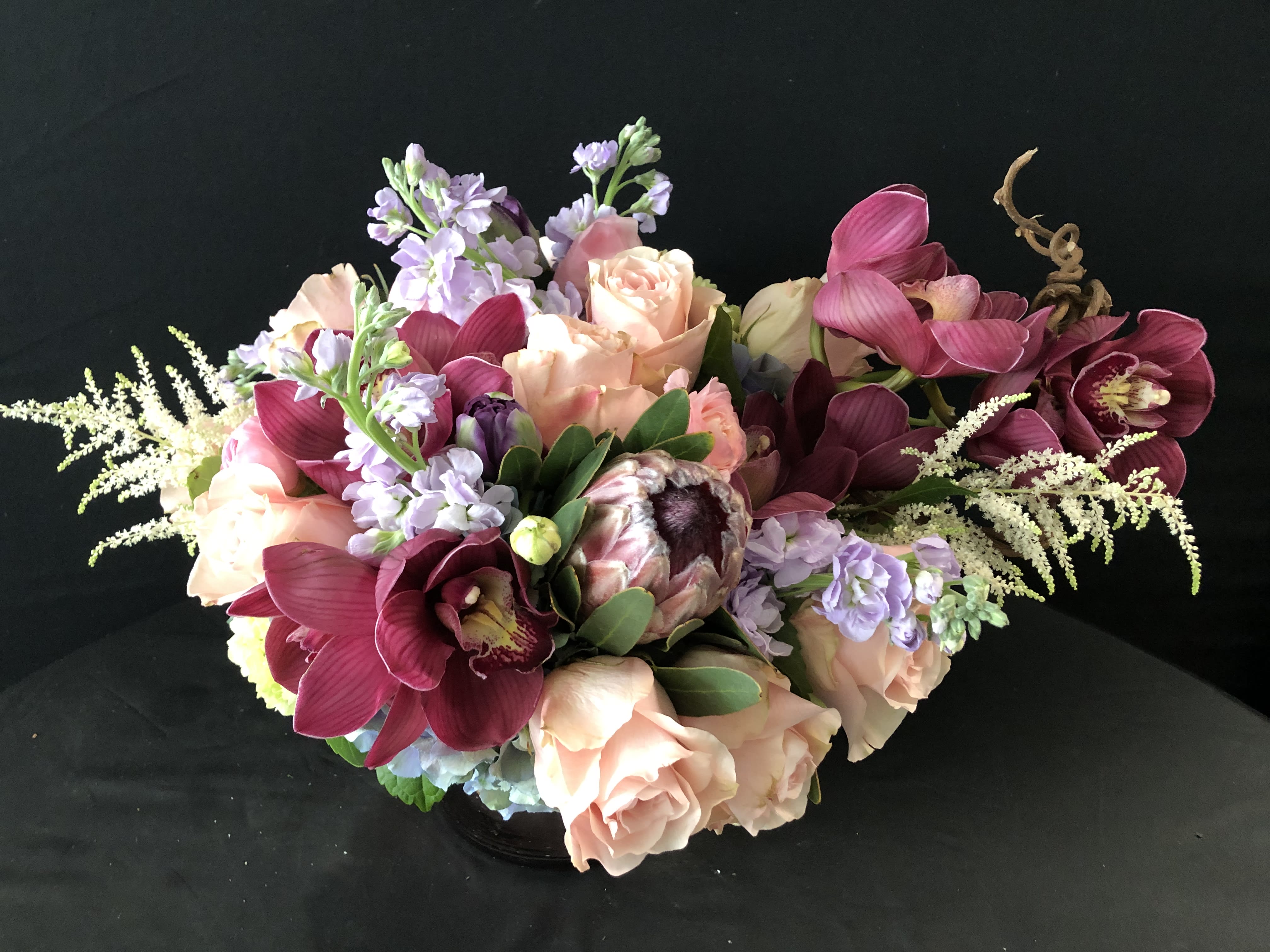 Bouquet of peach roses, burgundy orchids, and lavender flowers