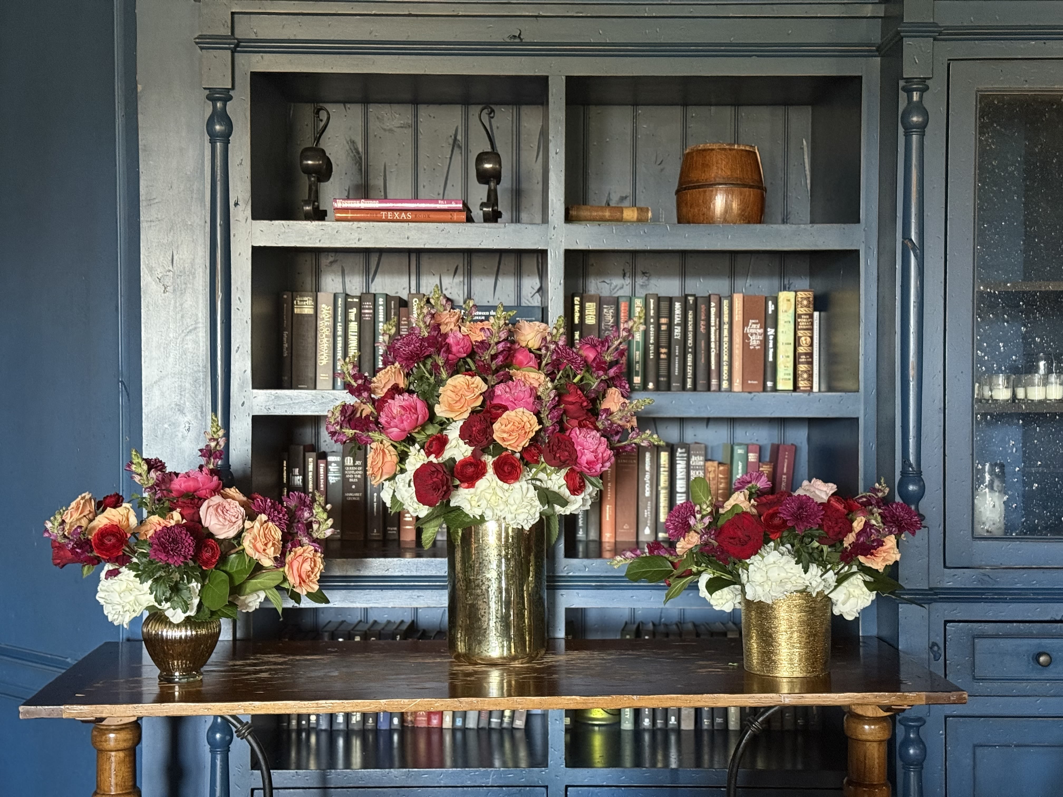 Three floral arrangements in gold vases on a table