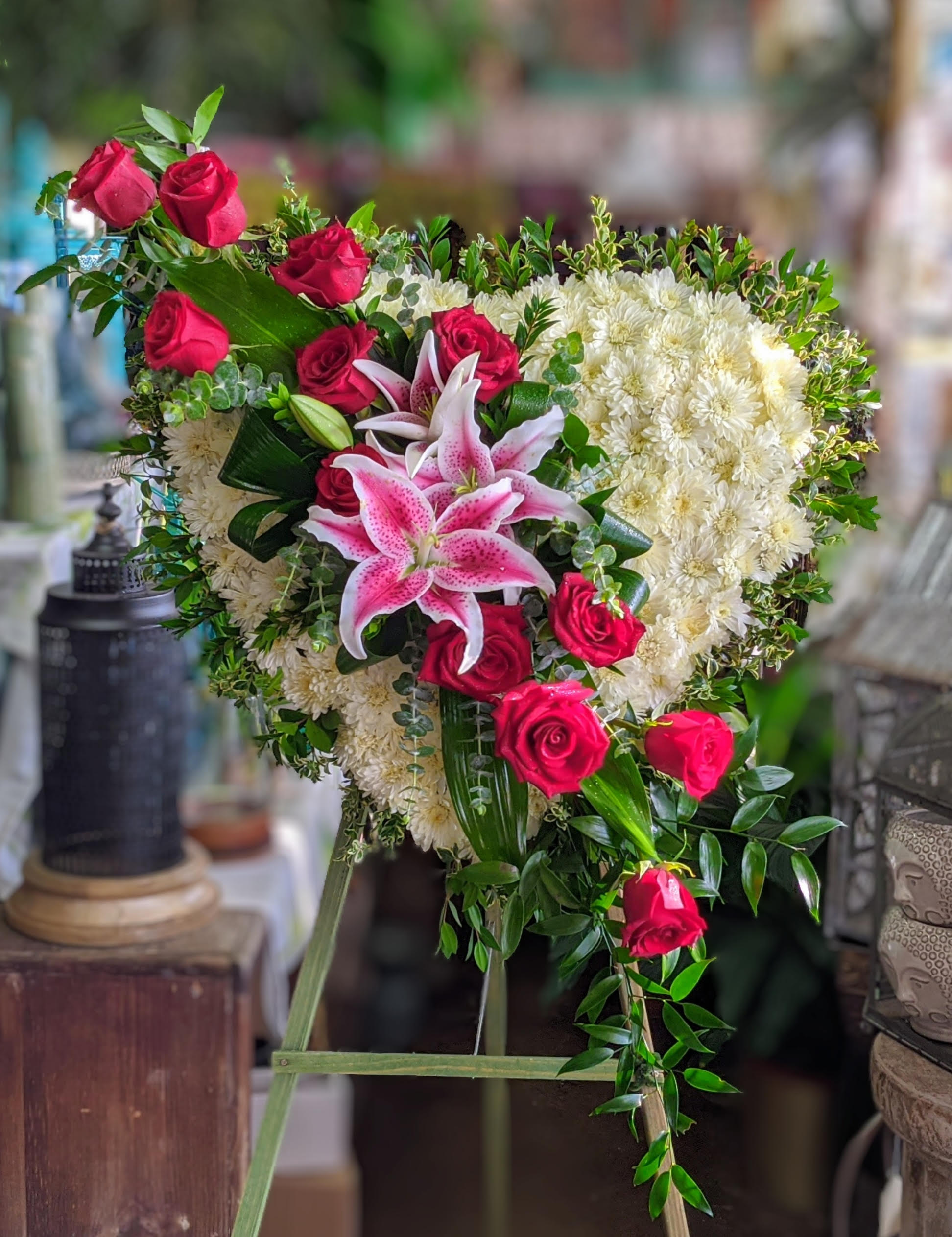True Heart Standing Spray - True Heart by Windmill Floral Expressions, Las Vegas  A radiant symbol of unwavering love and remembrance, True Heart is a striking floral tribute that speaks directly from the soul. Handcrafted in the shape of a heart, this design features a base of soft ivory blooms surrounded by fresh greenery, adorned with bold red roses and dramatic stargazer lilies—each flower representing deep passion, devotion, and eternal connection.  Perfect for memorial services or heartfelt farewells, True Heart by Windmill Floral Expressions in Las Vegas is a powerful expression of love that endures beyond words. Its beauty, elegance, and sincerity create a lasting impression of honor, affection, and everlasting bond.  