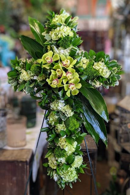 Verdant Cross - Verdant Cross by Windmill Floral Expressions, Las Vegas  Symbolizing eternal life, renewal, and deep spiritual peace, Verdant Cross is a lush and graceful floral tribute handcrafted in the sacred shape of a cross. Designed with an abundance of green hydrangea, cymbidium orchids, mossy green trick, and rich tropical foliage, this arrangement captures the essence of tranquility and reverence.  Verdant Cross from Windmill Floral Expressions in Las Vegas offers a meaningful and serene gesture of faith—perfect for memorial services, celebrations of life, or religious ceremonies. Its natural green palette reflects growth, hope, and everlasting devotion, making it a heartfelt expression of love and remembrance.