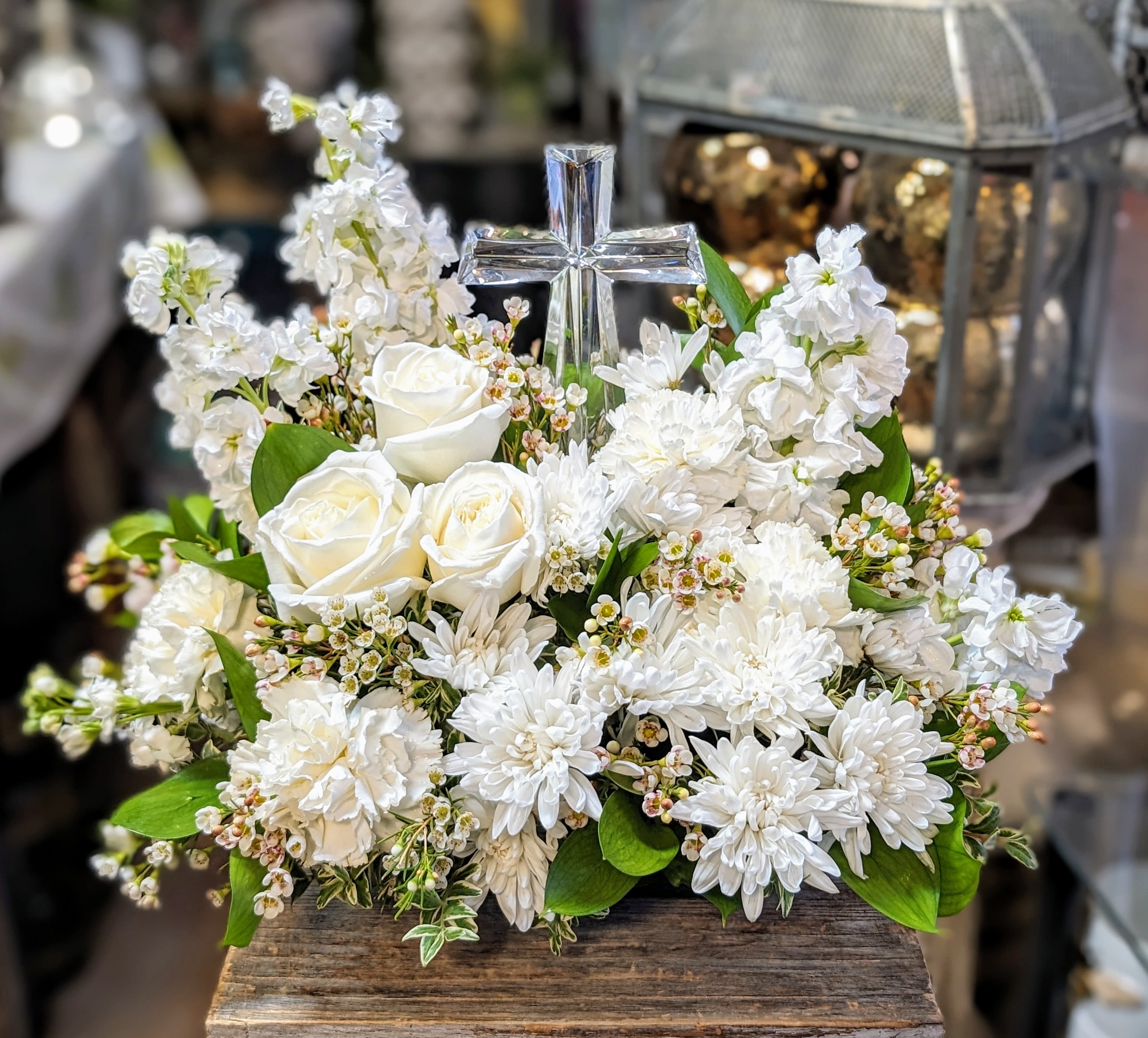 White floral arrangement with roses, daisies, and a clear glass cross