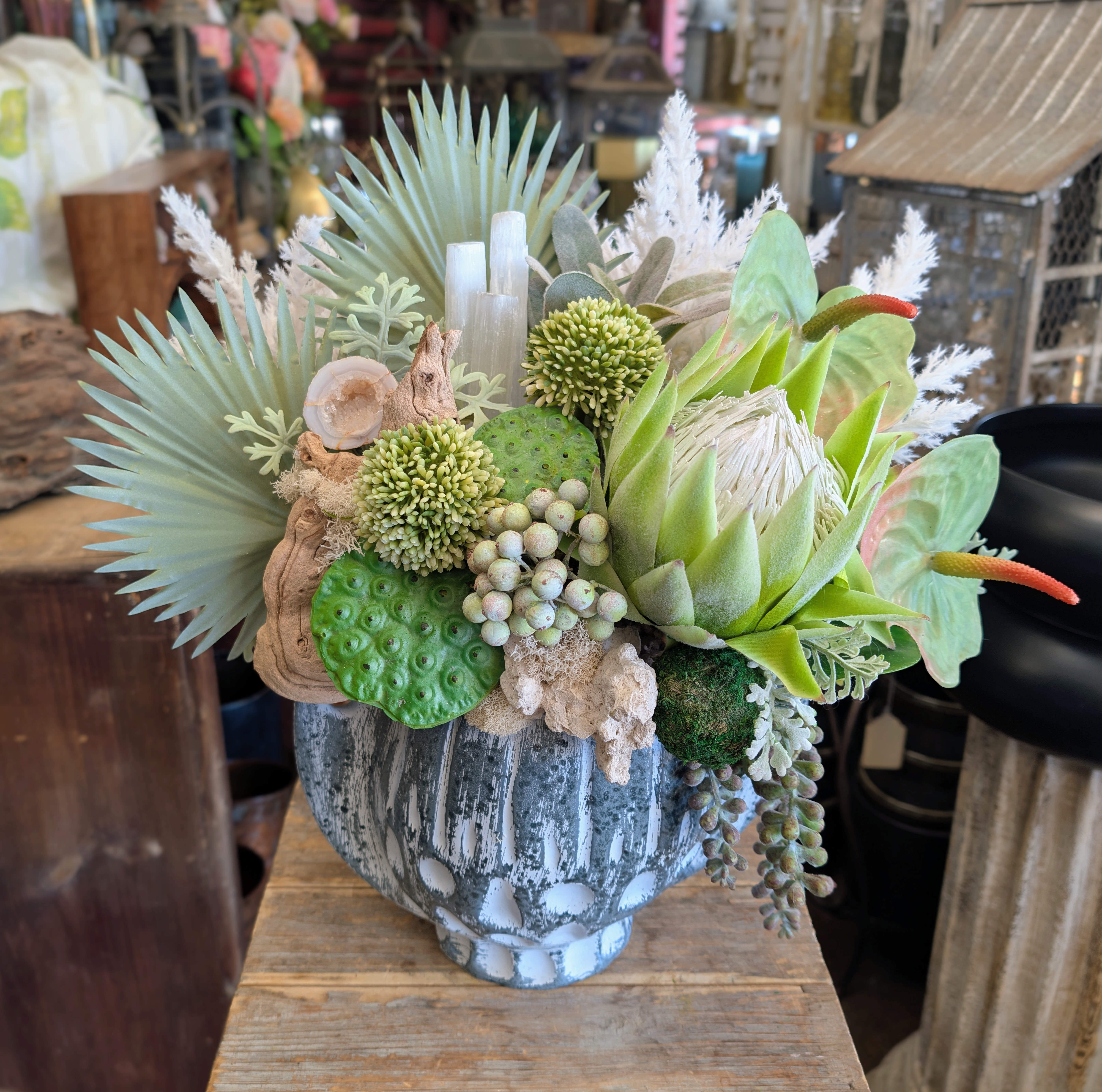 Succulent arrangement in a weathered gray vase with pale green and white accents.